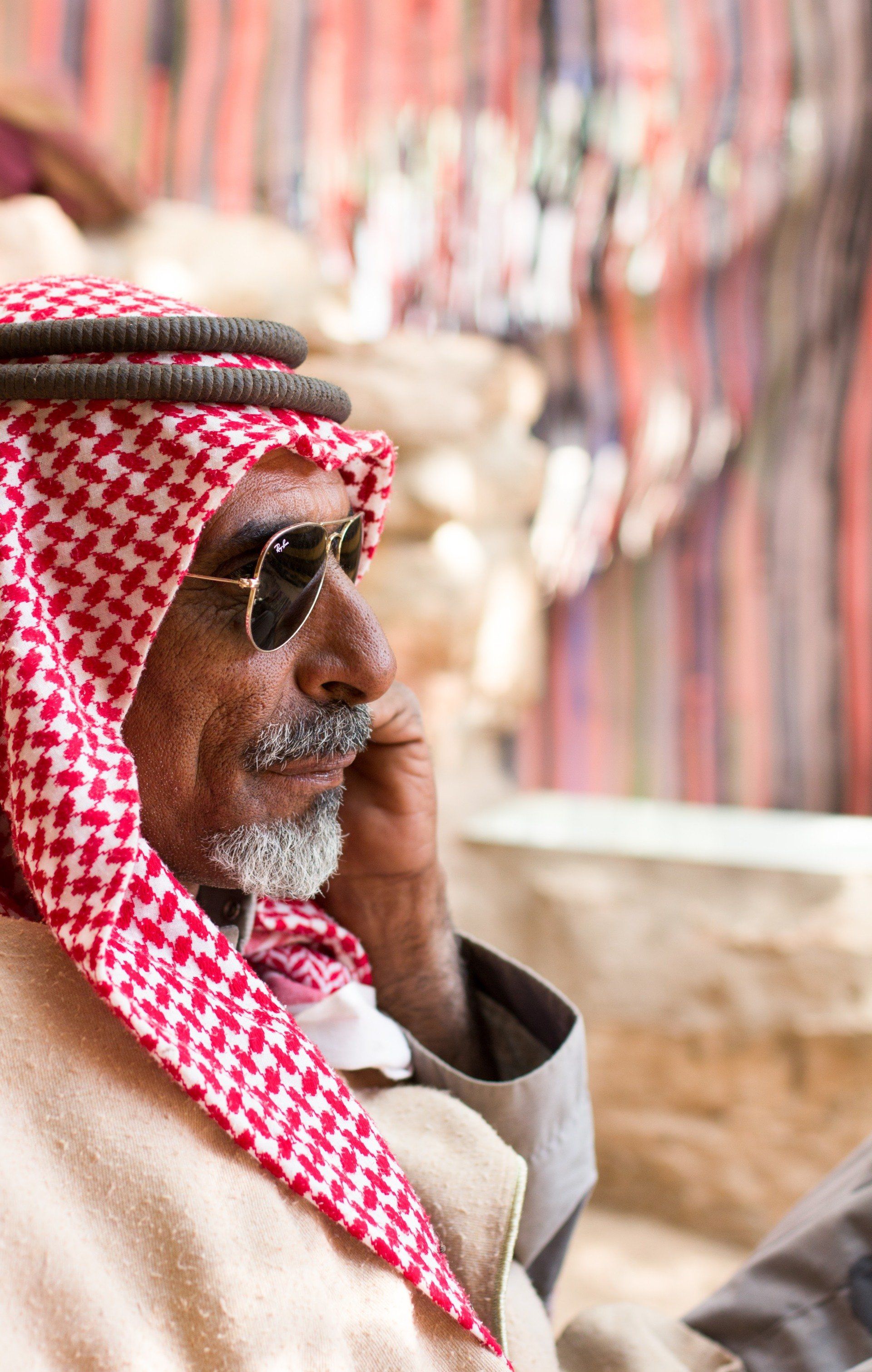 A man wearing a keffiyeh and sunglasses is talking on a cell phone.