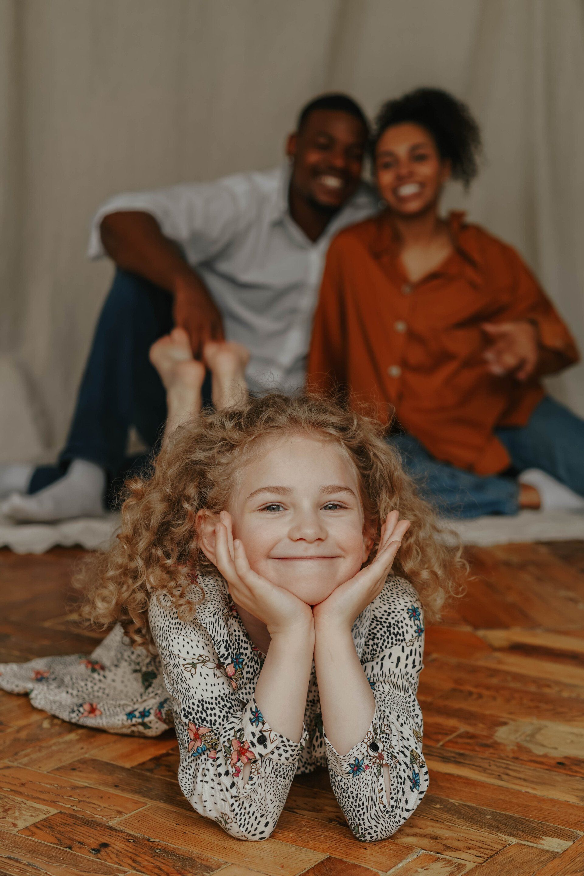 A little girl is laying on the floor with her parents in the background.