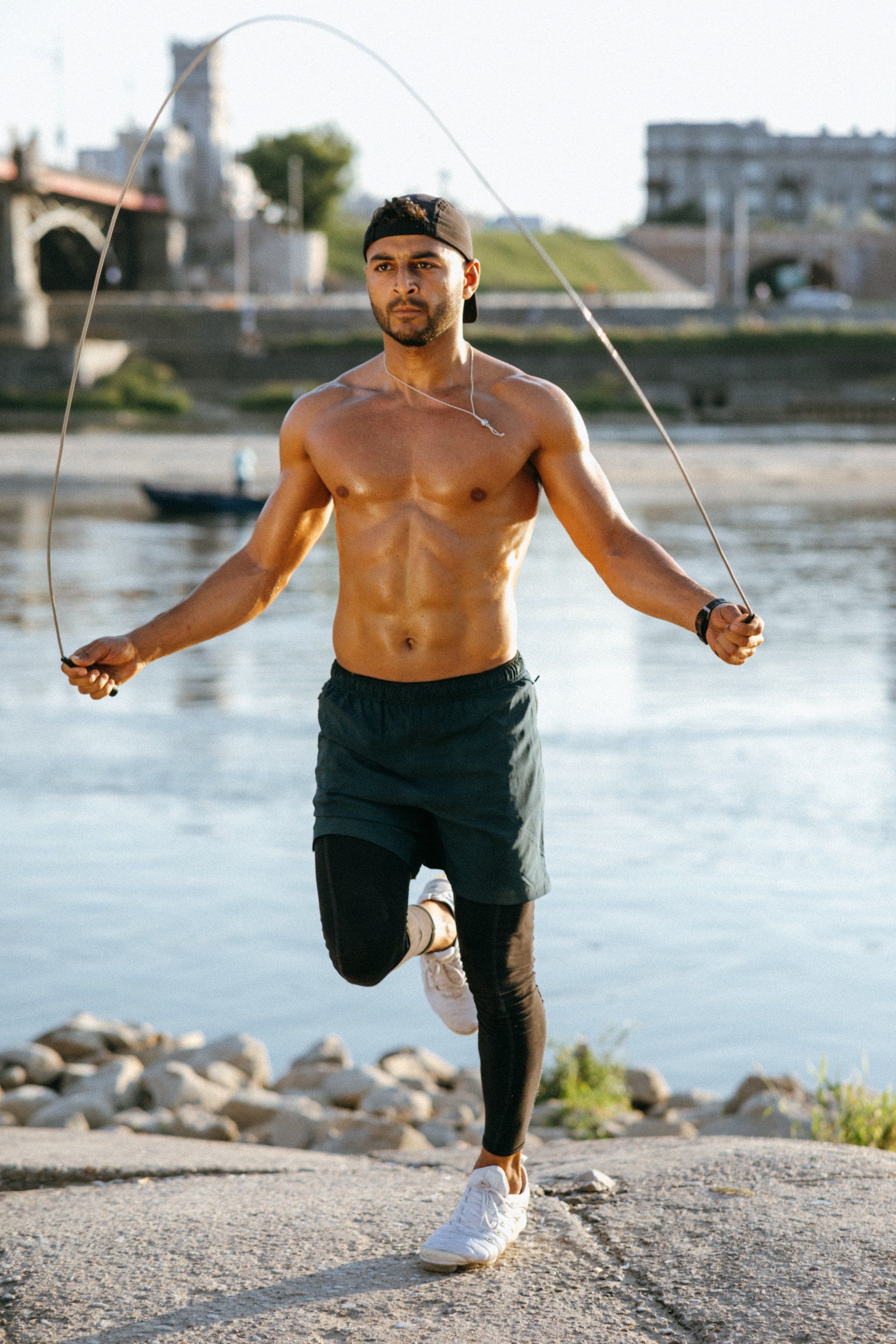 a shirtless man is jumping a jump rope in front of a river .