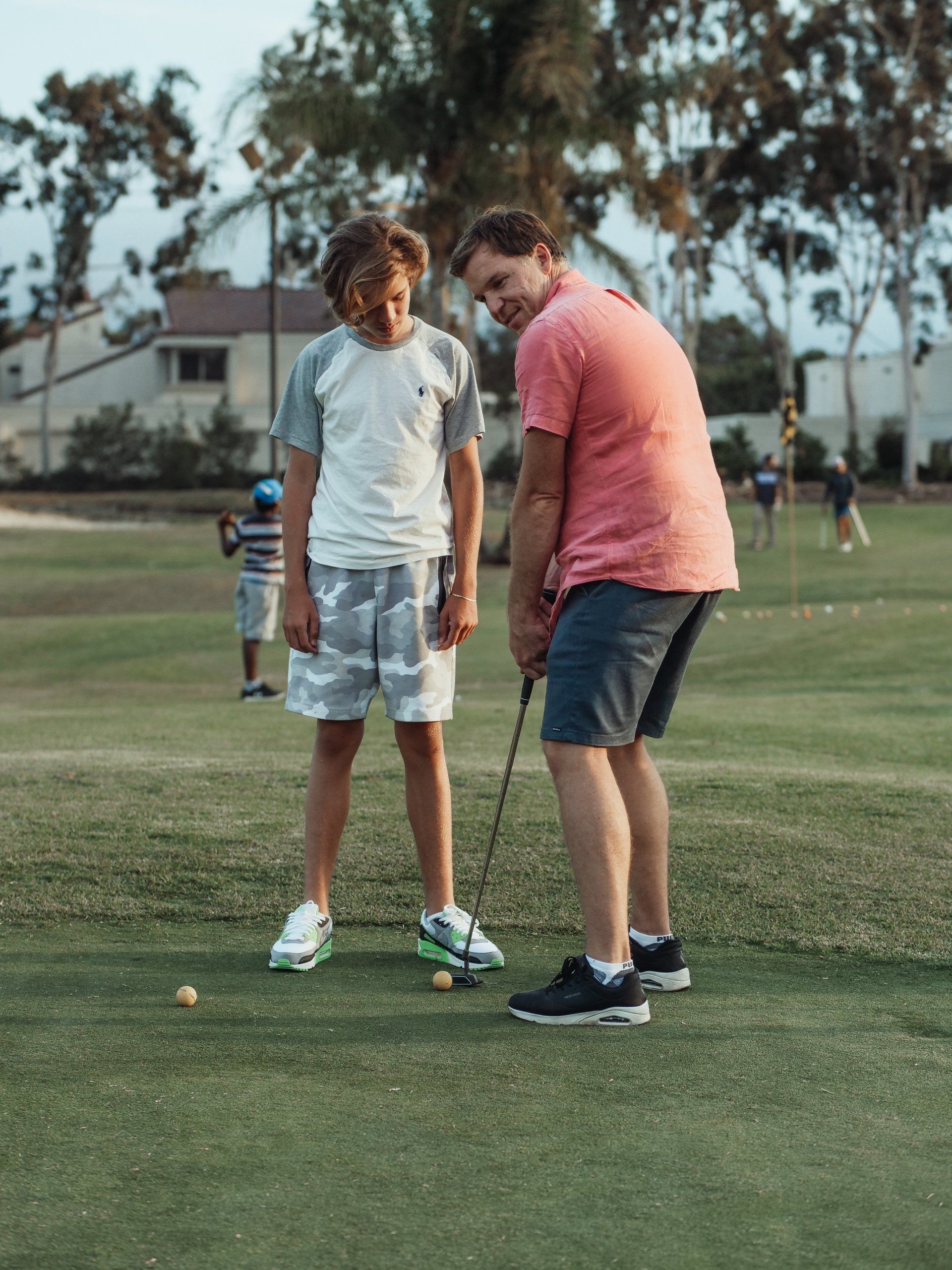 A man is teaching a young boy how to play golf.