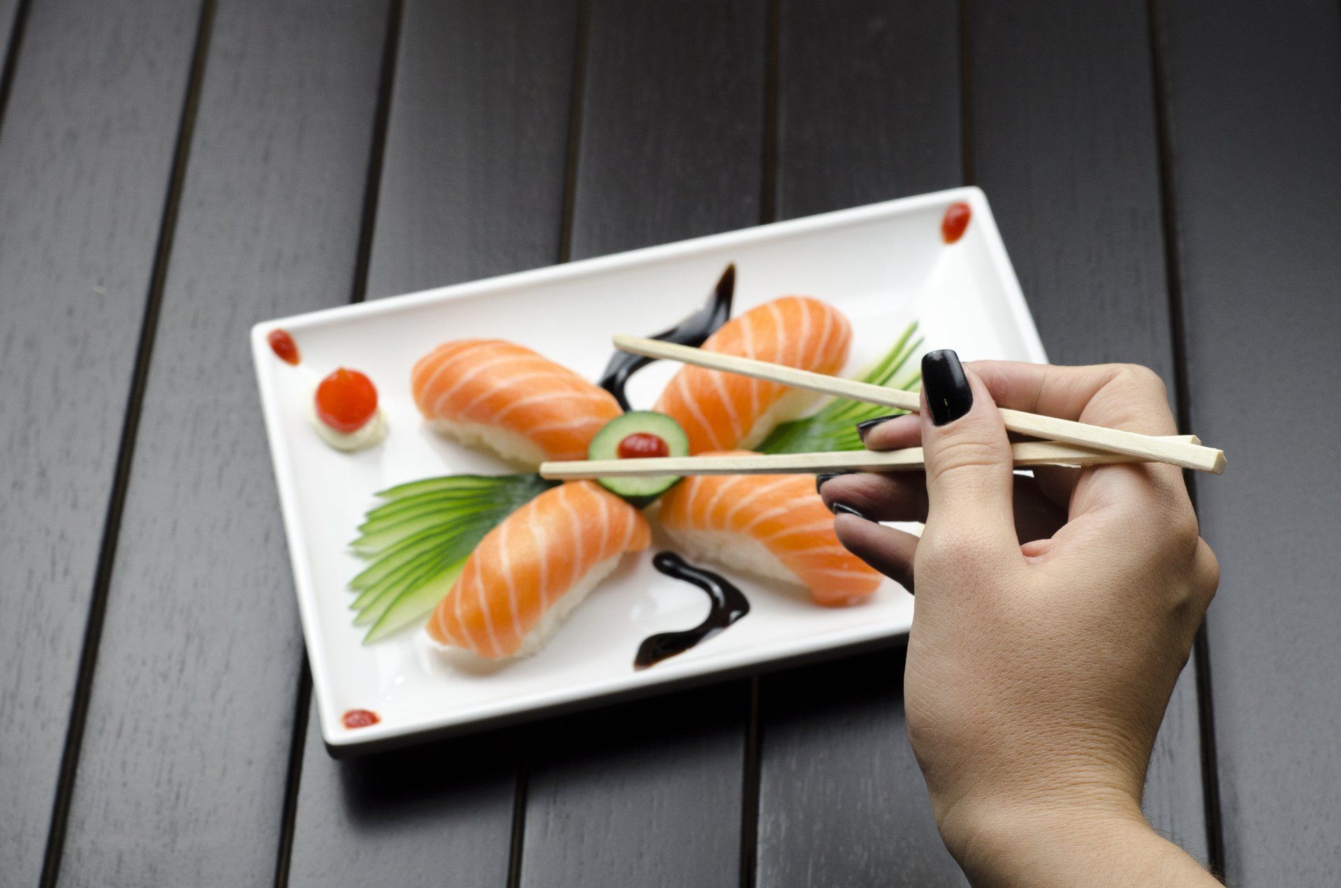 A person is holding chopsticks over a plate of sushi