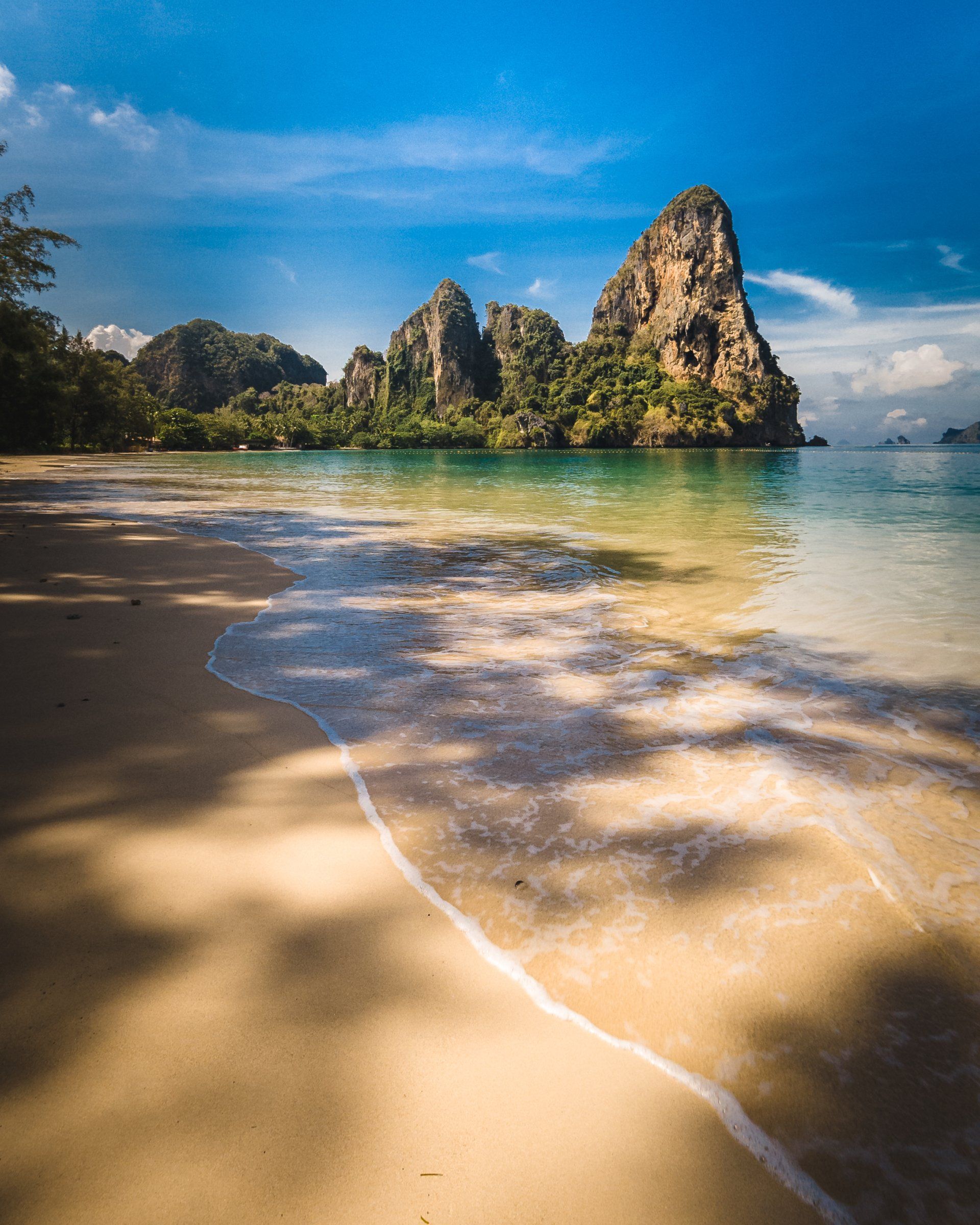 A beach with a mountain in the background and waves crashing on the sand.