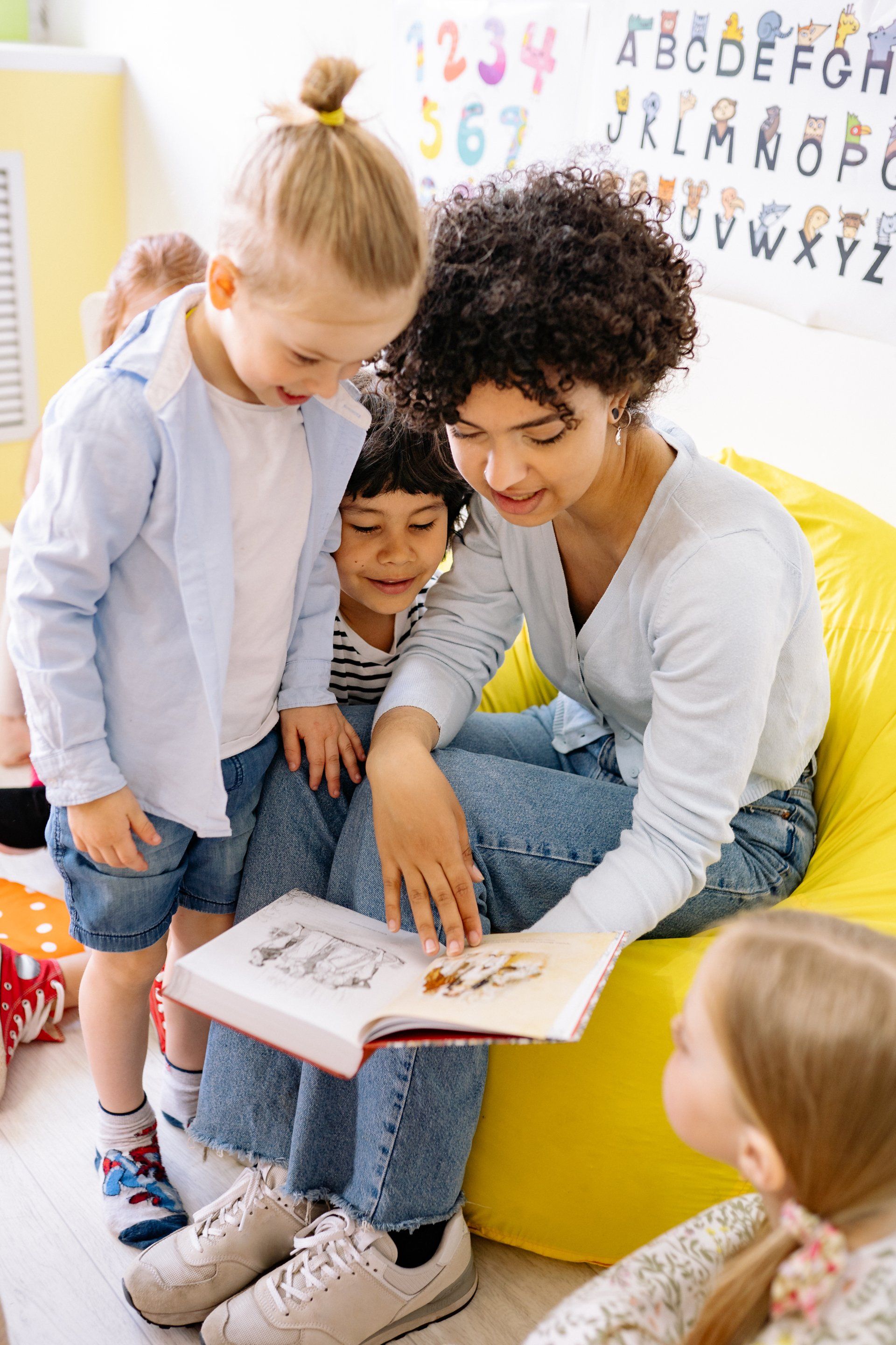 A woman is sitting on a bean bag chair reading a book to two children.