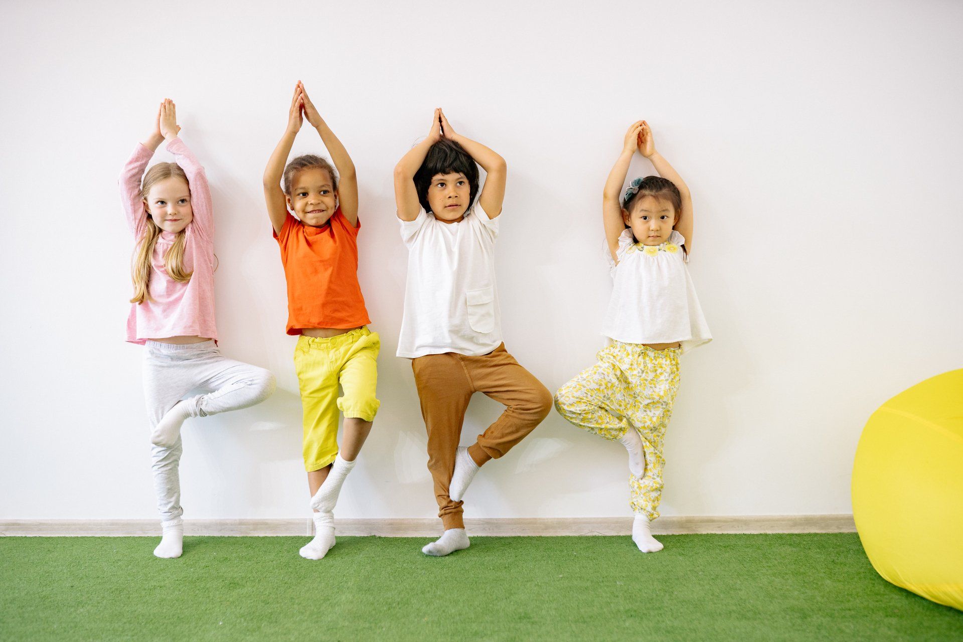 Four children lined up against a wall doing a yoga pose