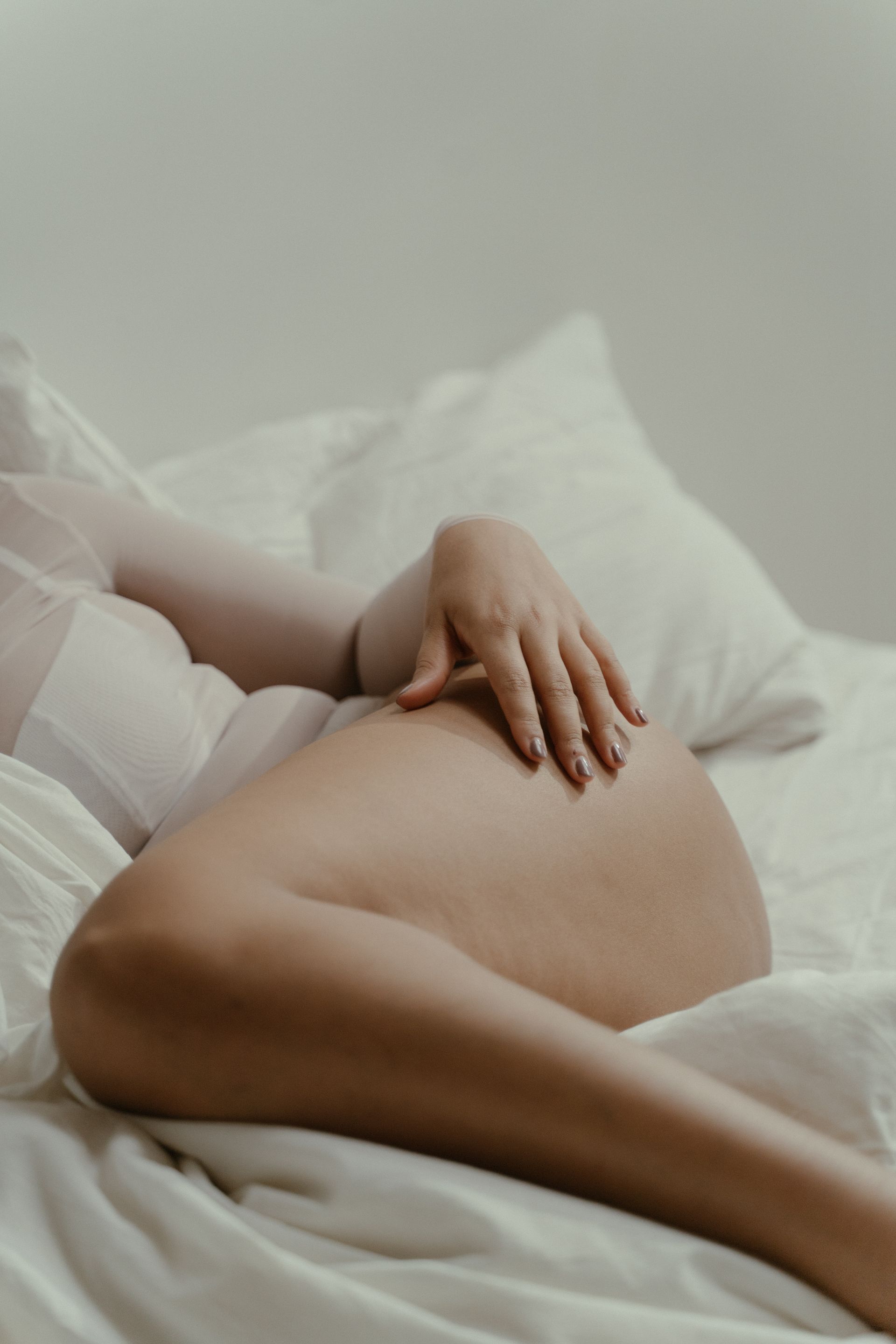 A pregnant woman is laying on a bed with her hands on her belly.