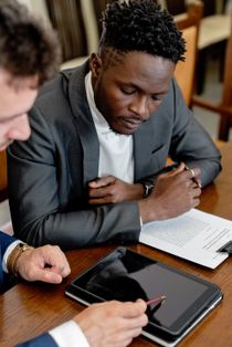 Two men are sitting at a table looking at a tablet.