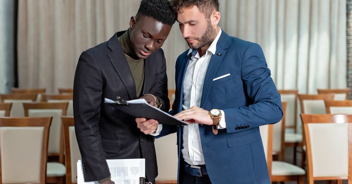 Dois homens de terno estão olhando para uma prancheta em uma sala de conferências.