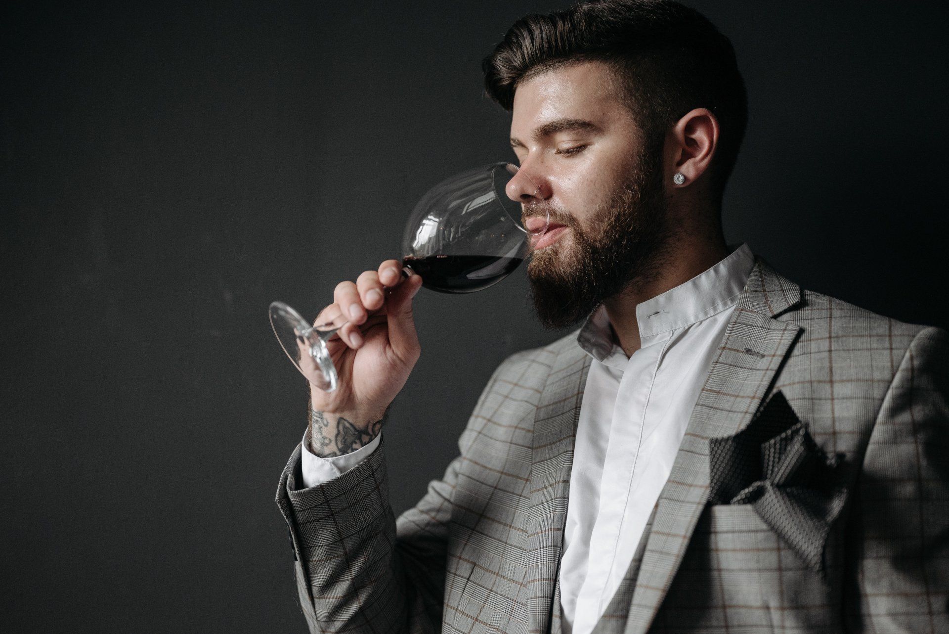 A man in a suit is drinking a glass of red wine.