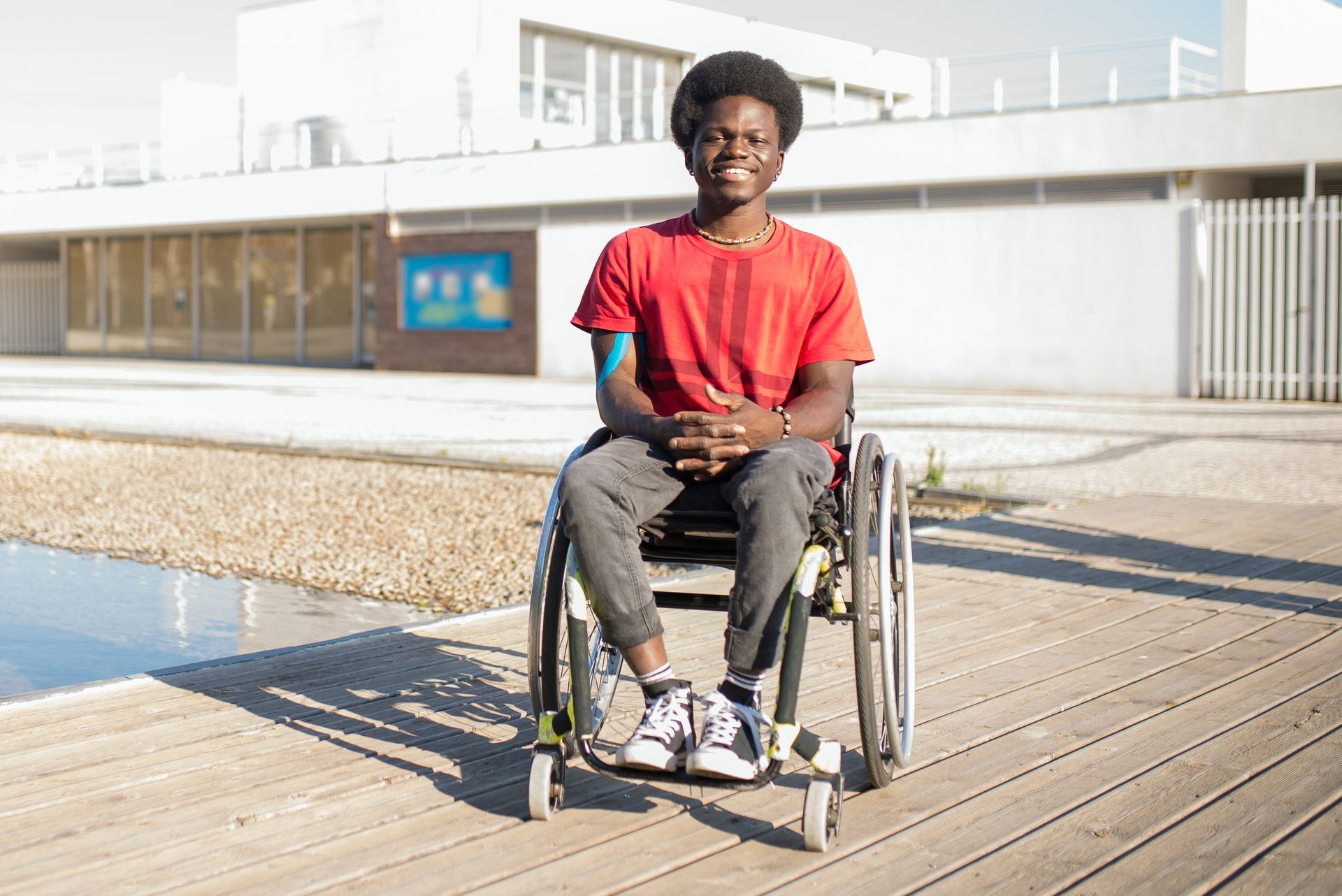 A young man is sitting in a wheelchair on a wooden deck.