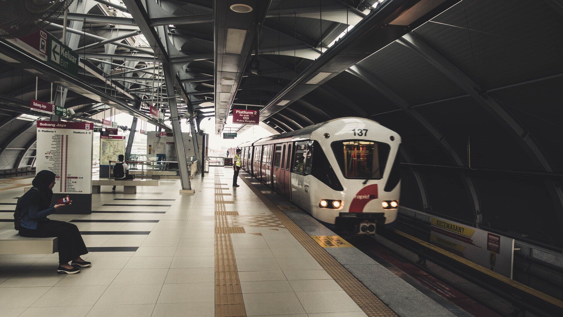 A woman is sitting on a bench at a train station waiting for the train to arrive.