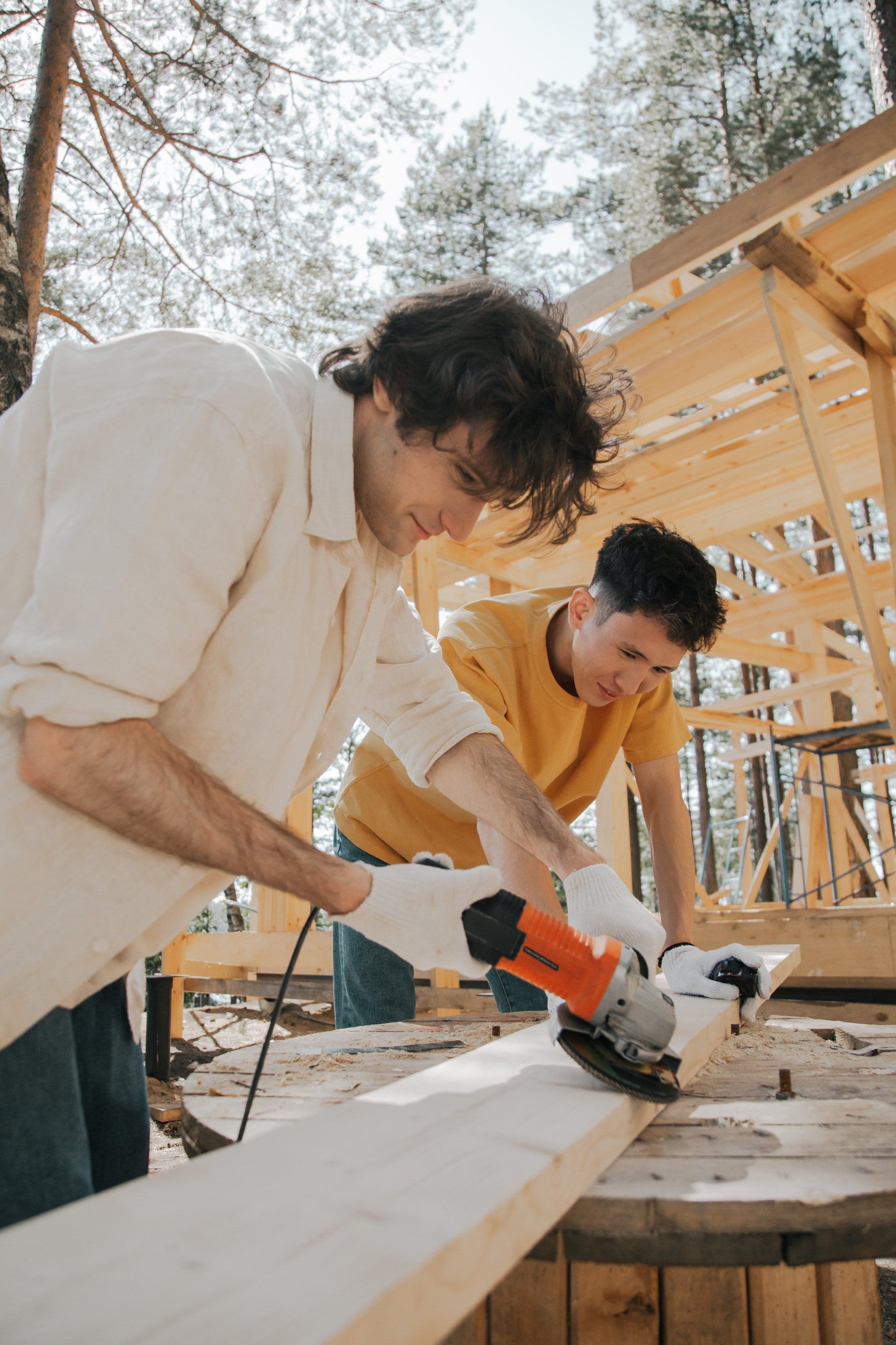 Two men working with power tools on a wooden board. 