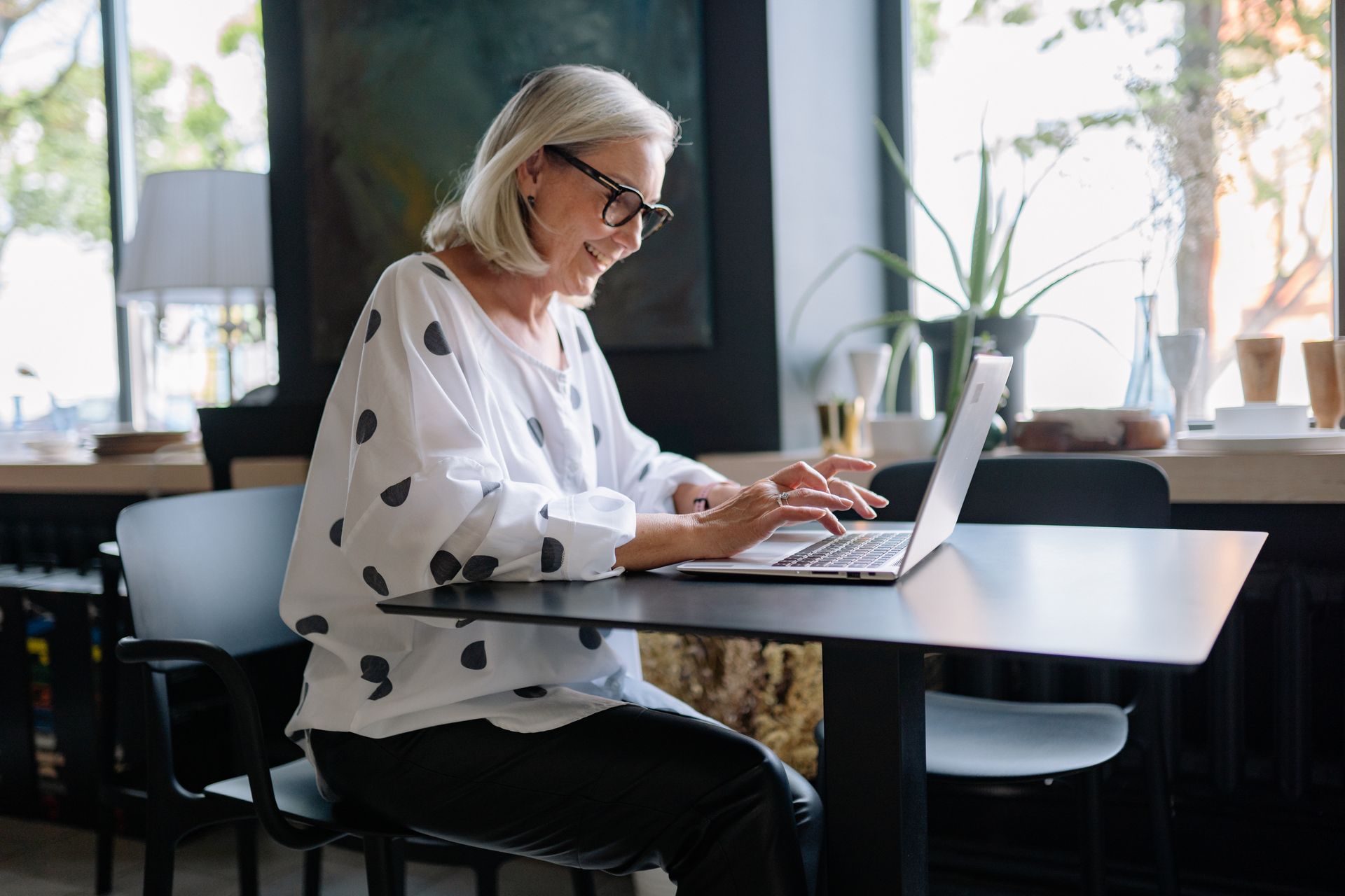 An older woman is sitting at a table using a laptop computer.