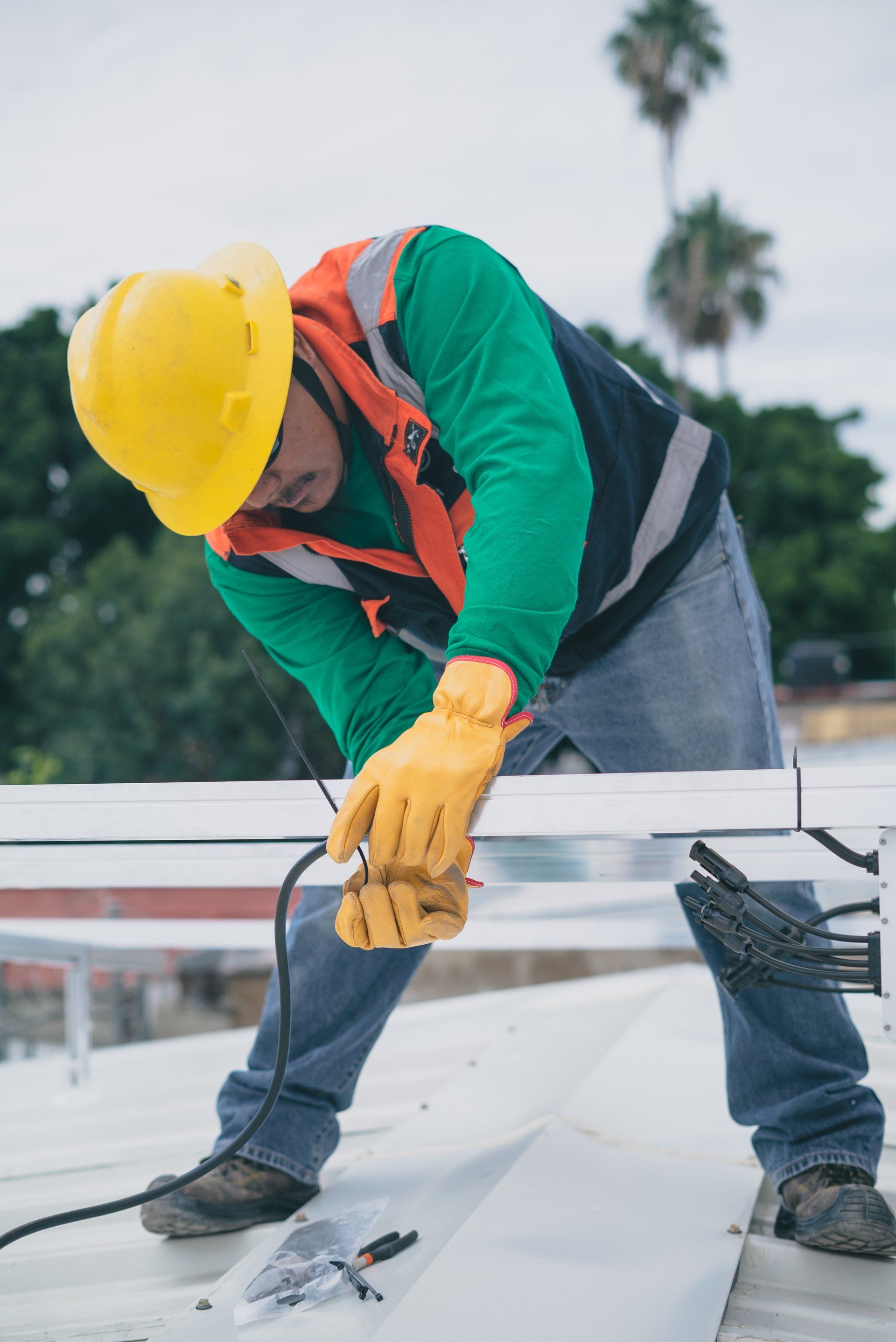 A man wearing a hard hat and gloves is working on a roof.