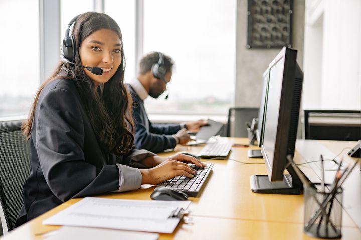 A woman wearing a headset is sitting at a desk in front of a computer.