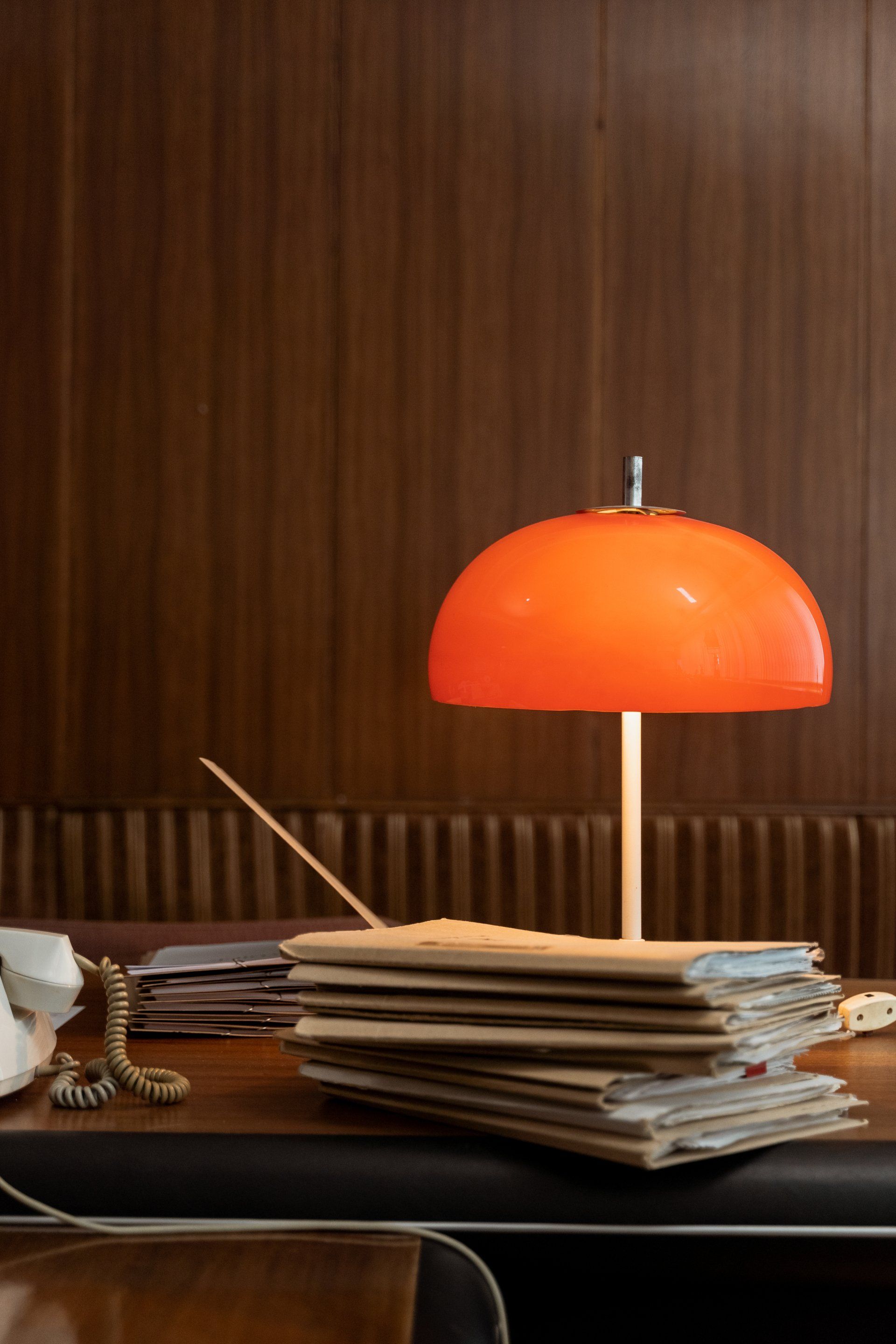 An orange lamp is sitting on top of a stack of papers on a desk.