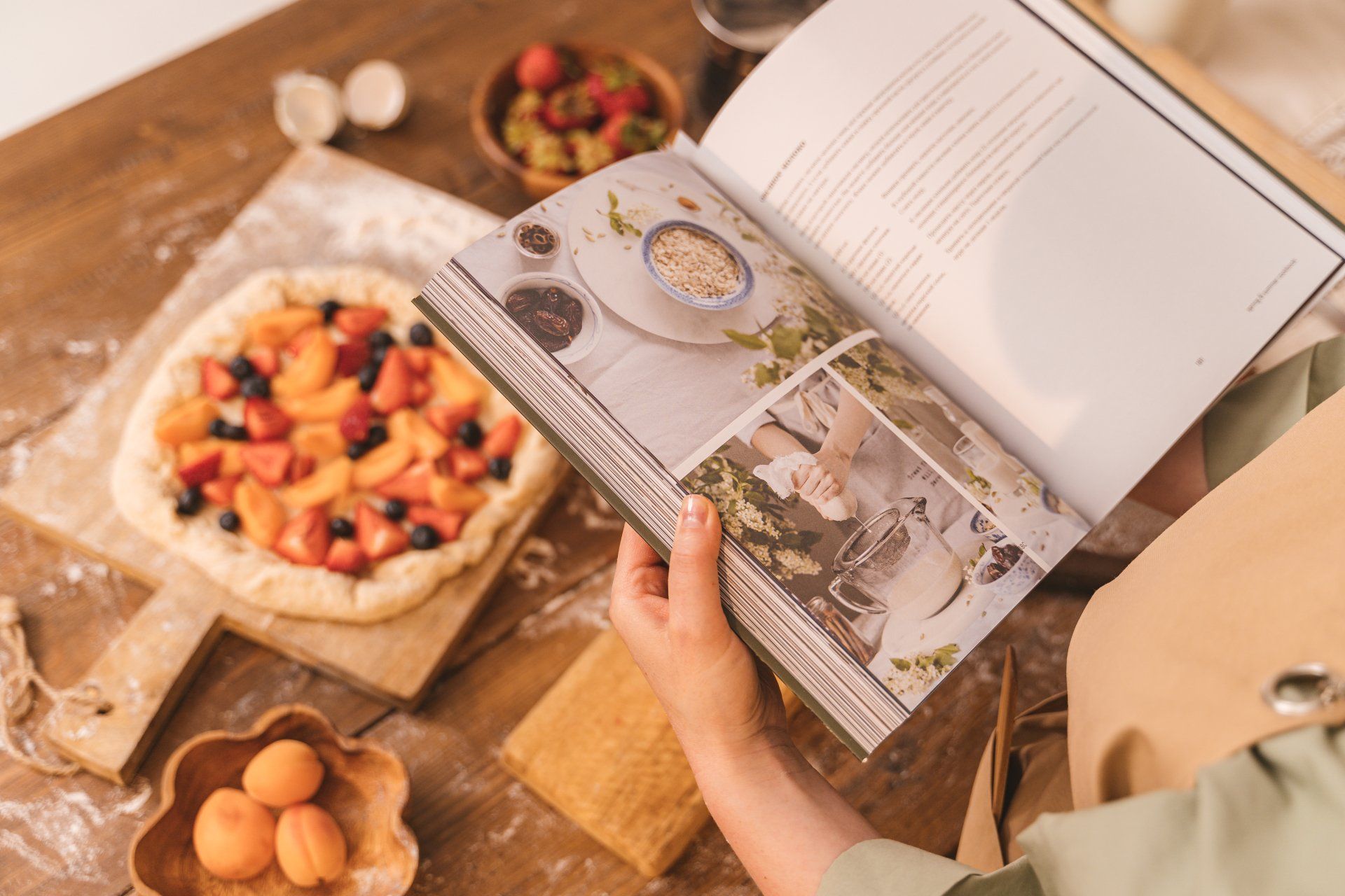 A person is reading a cookbook on a wooden table.