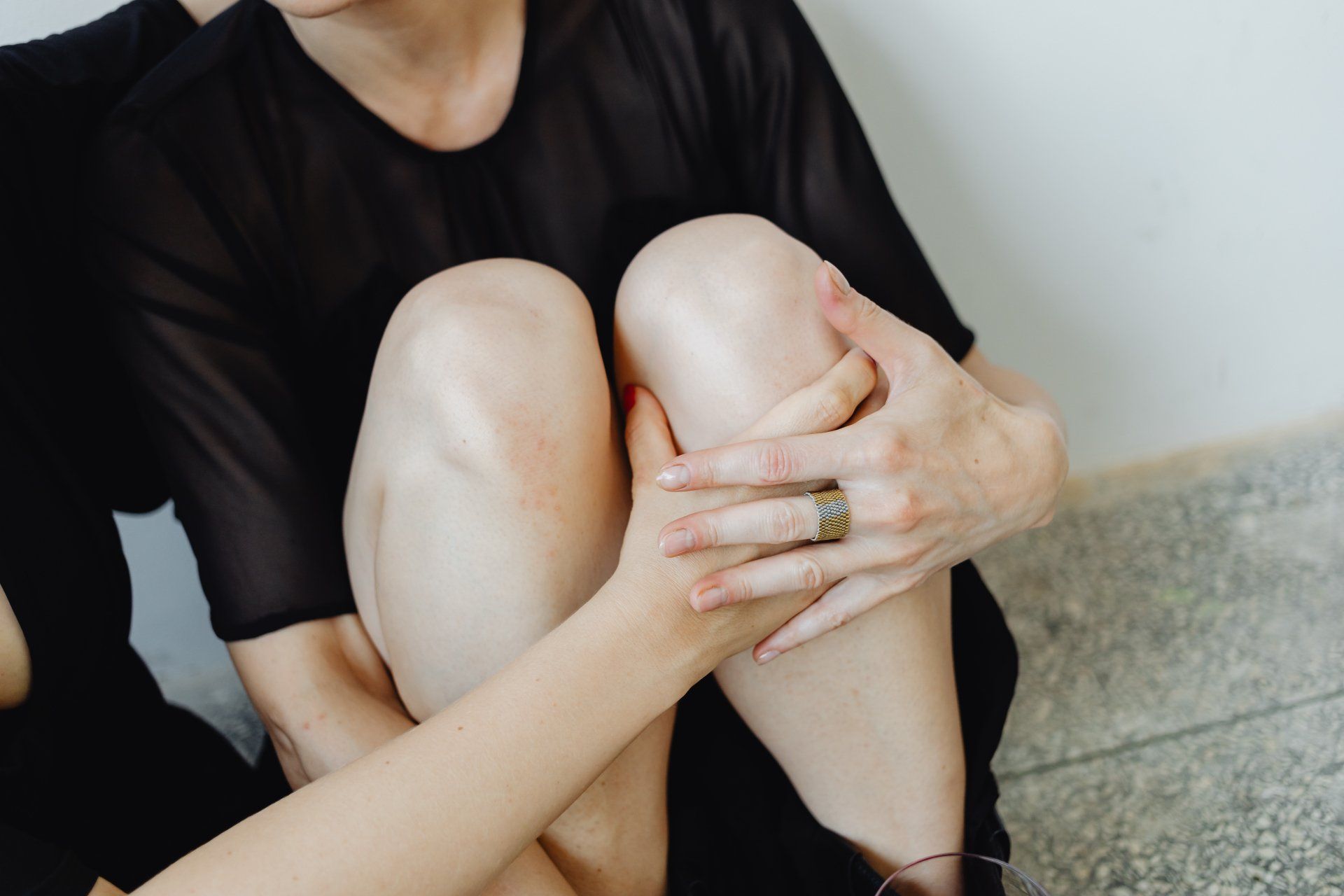 A woman in a black dress is sitting on the floor with her legs crossed.