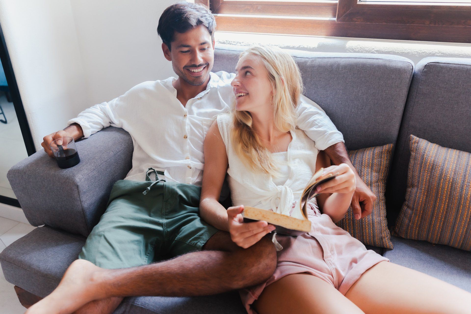 A man and a woman are sitting on a couch reading a book.