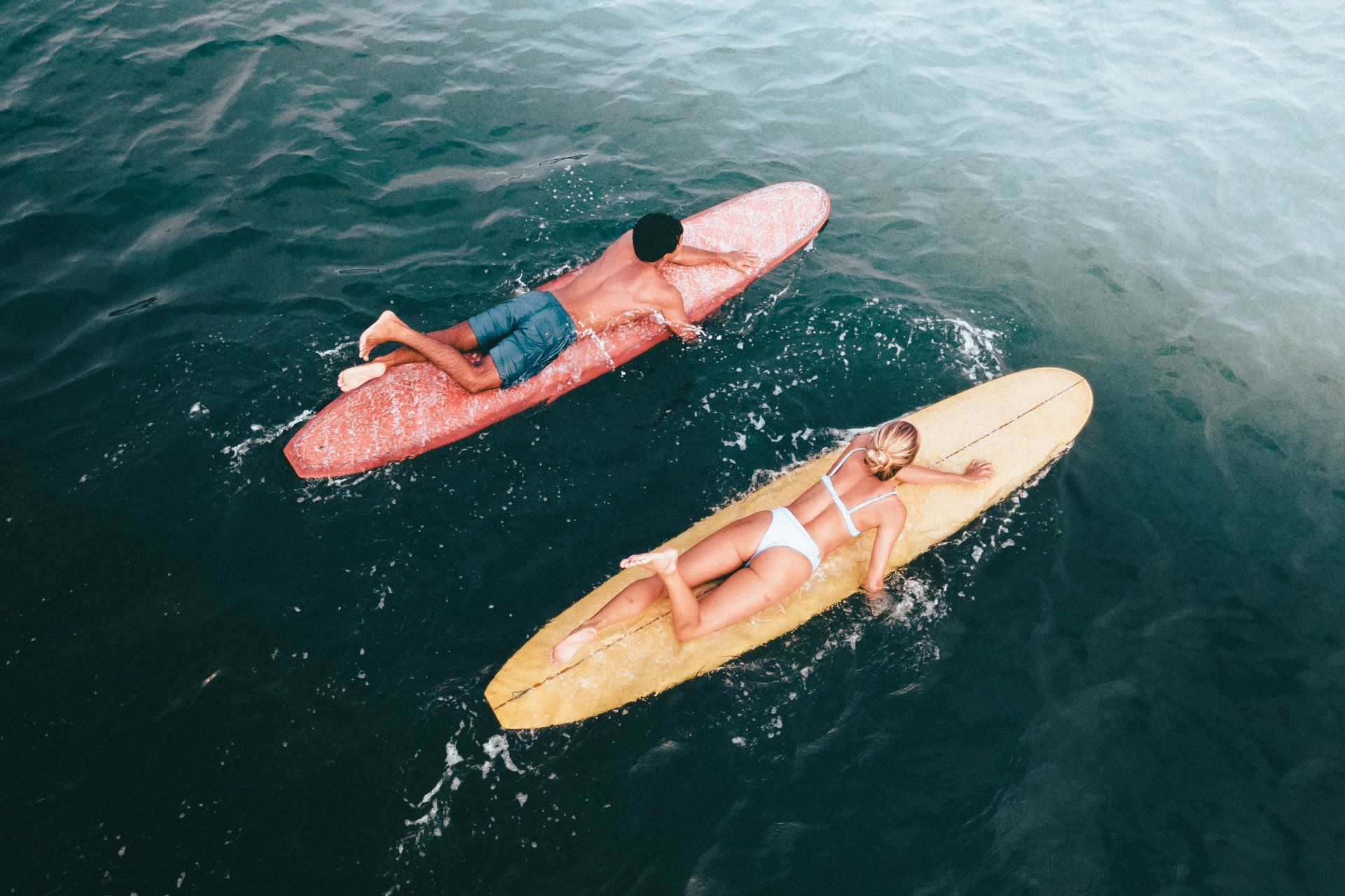 Un homme et une femme sont allongés sur des planches de surf dans l'océan lors d'une des retraites de Yoga