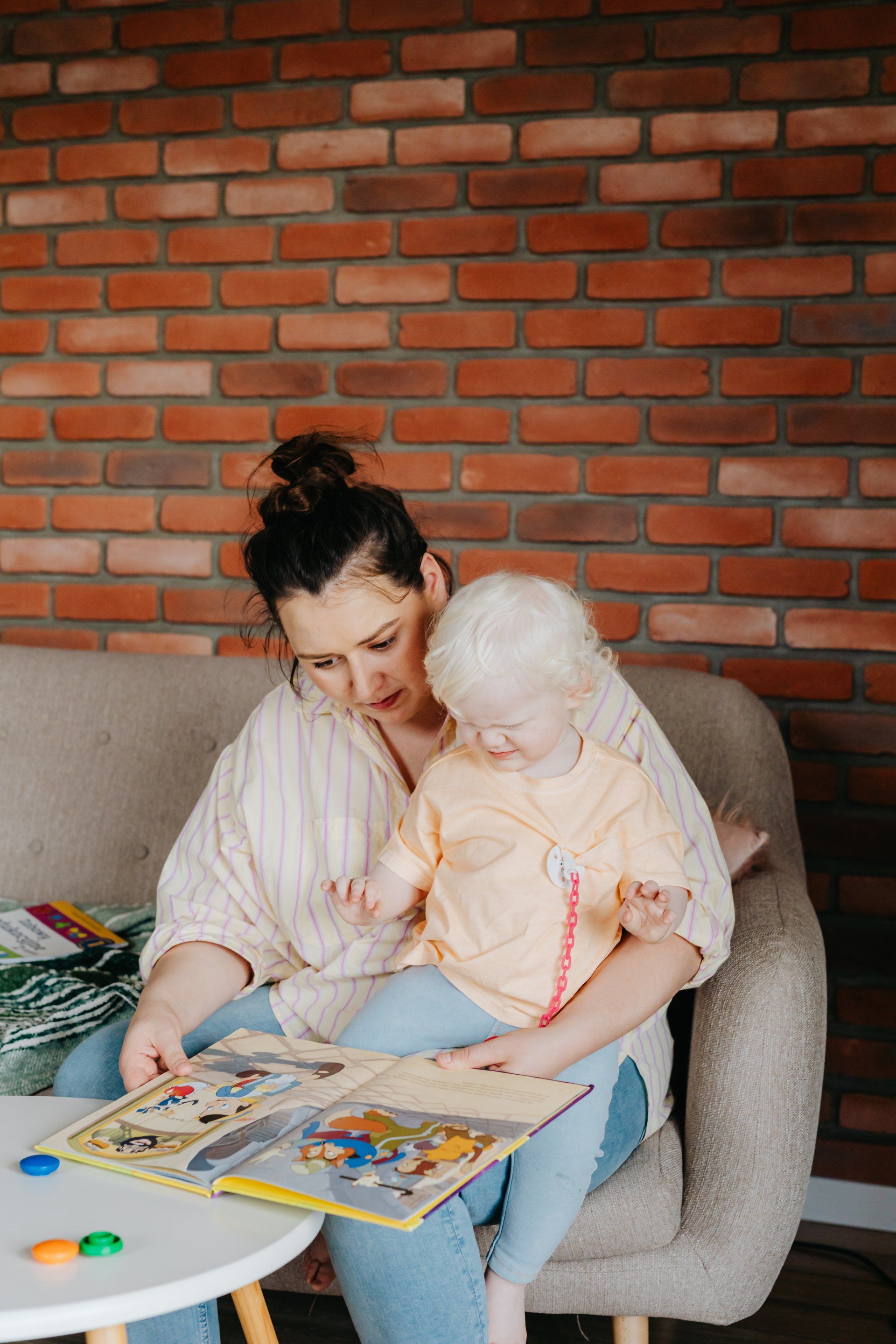 A woman is sitting on a couch reading a book to a baby.