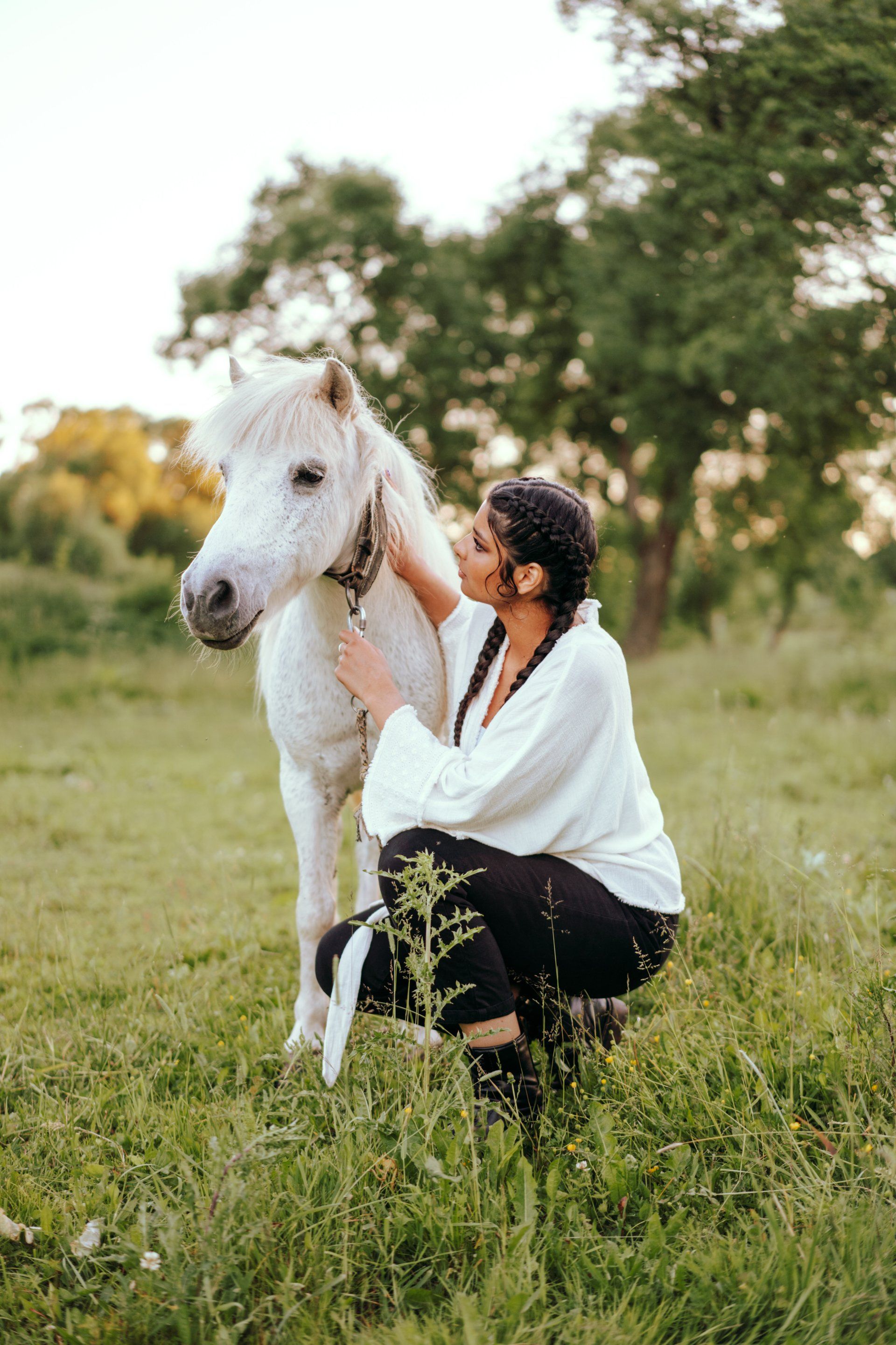 a woman is kneeling down next to a white horse in a field .