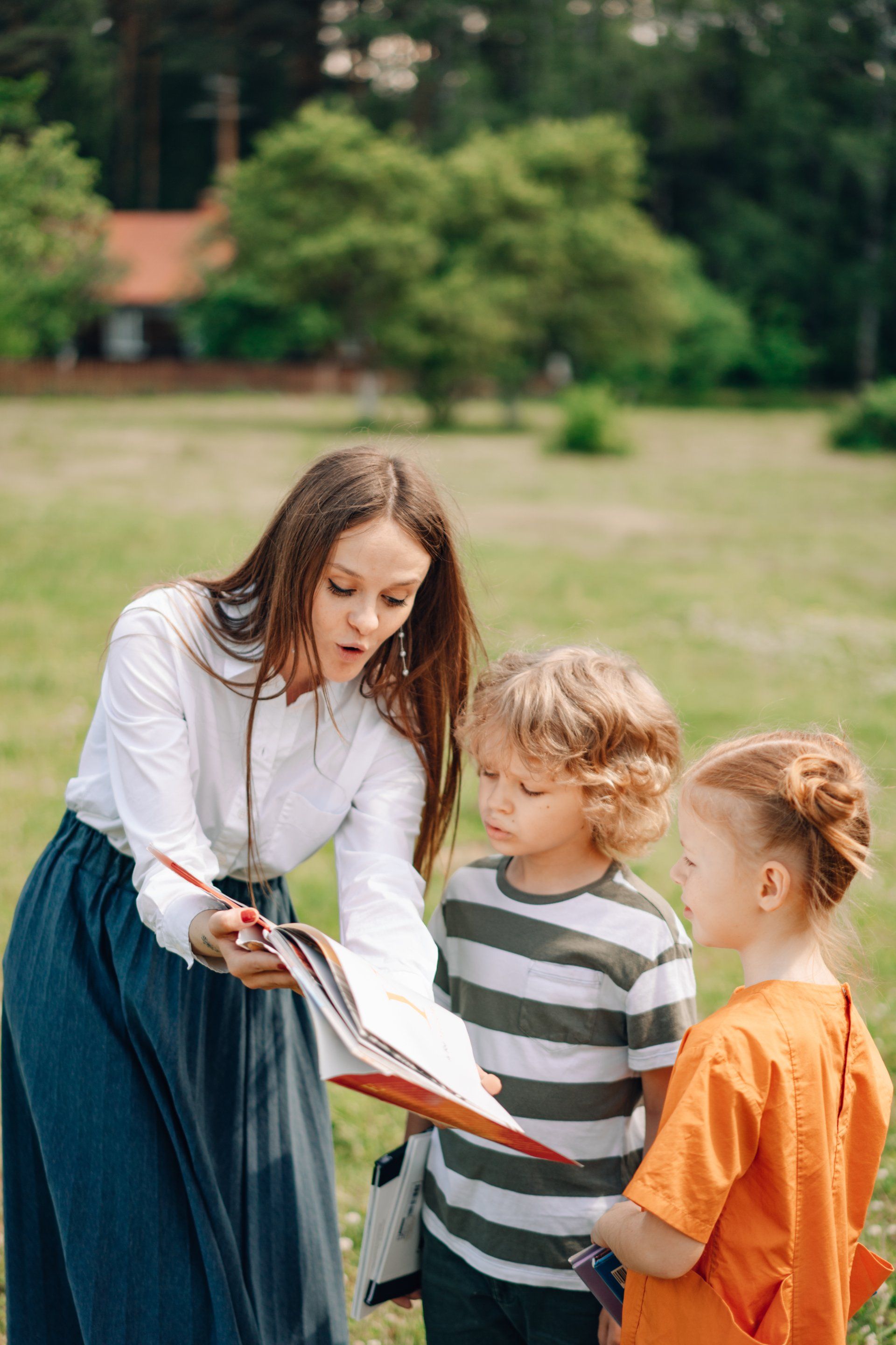 A woman is reading a book to two children in a park.