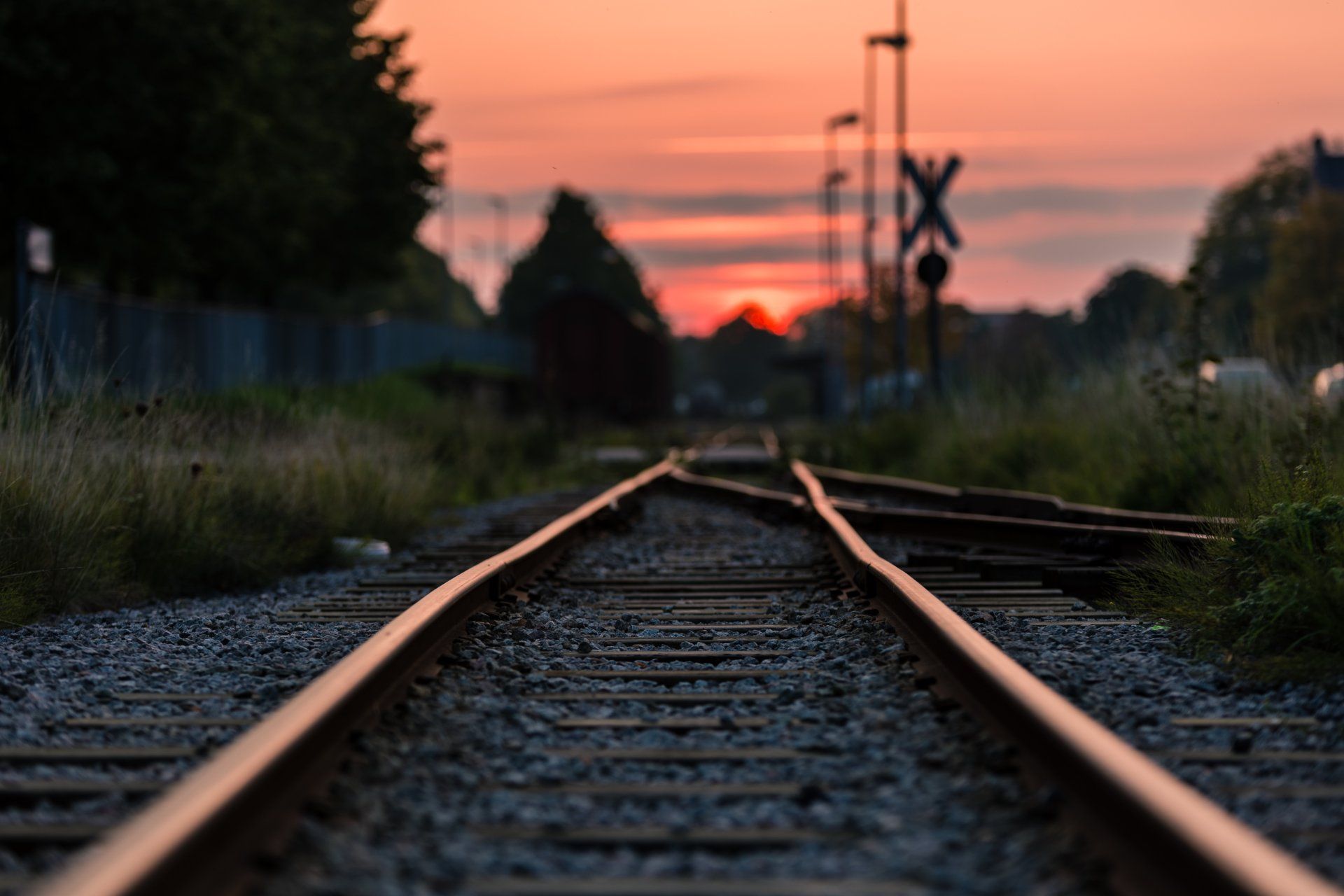 Railroad tracks leading toward a sunset, with a crossbuck sign visible.