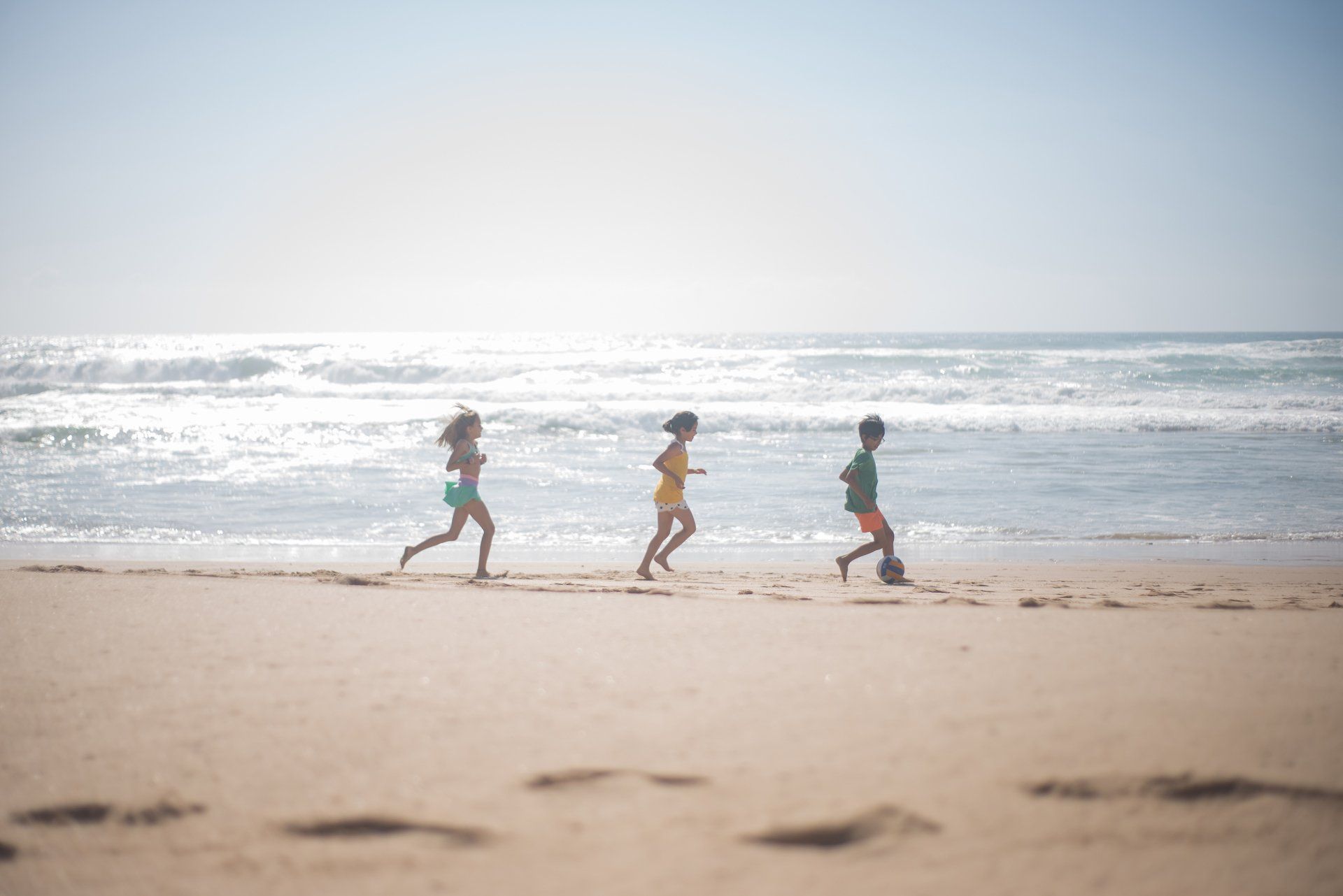 Three people are running on the beach near the ocean.