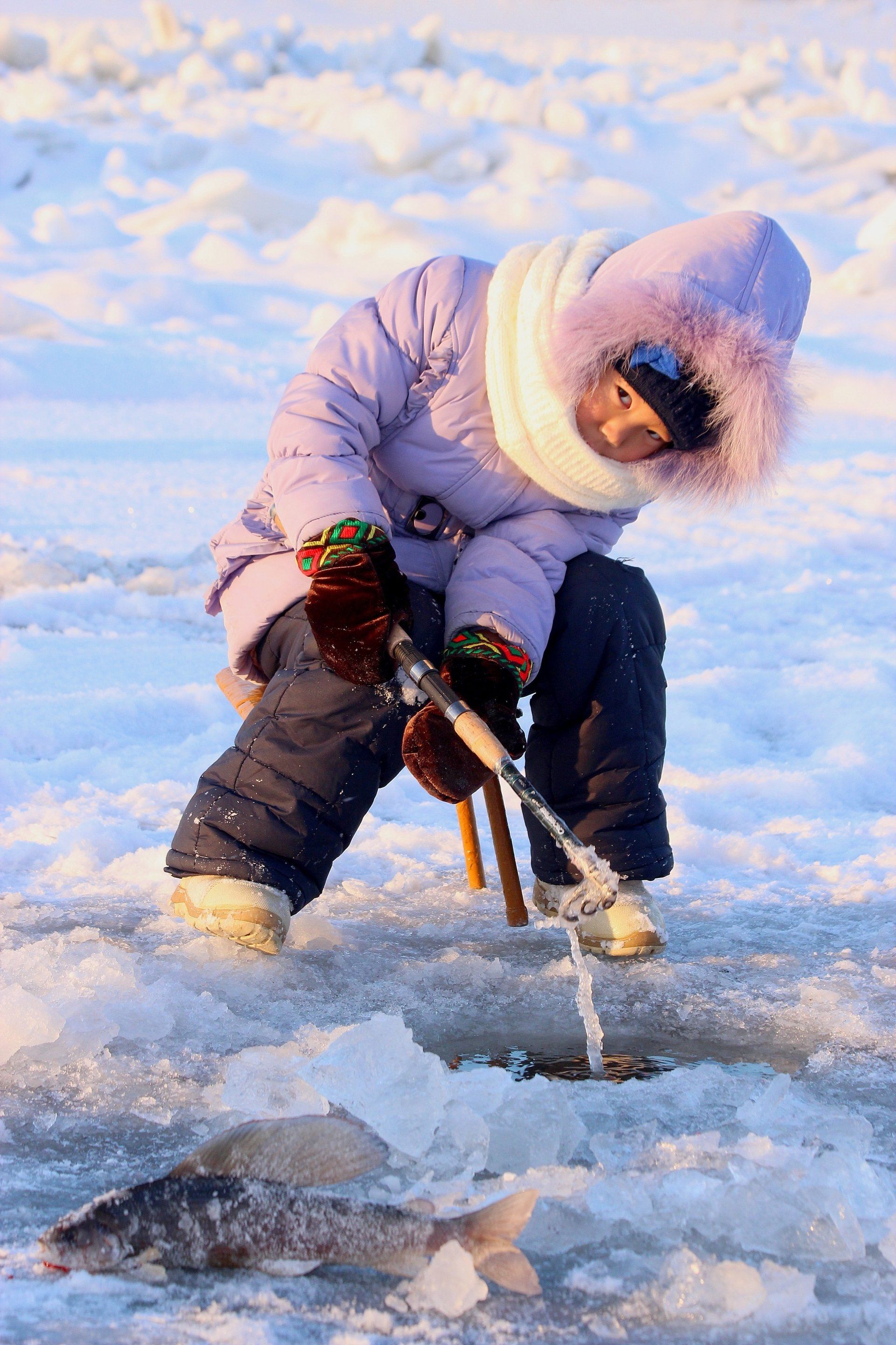 A little girl is ice fishing in the snow