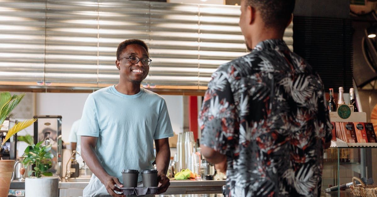 Two men are standing in a kitchen talking to each other.