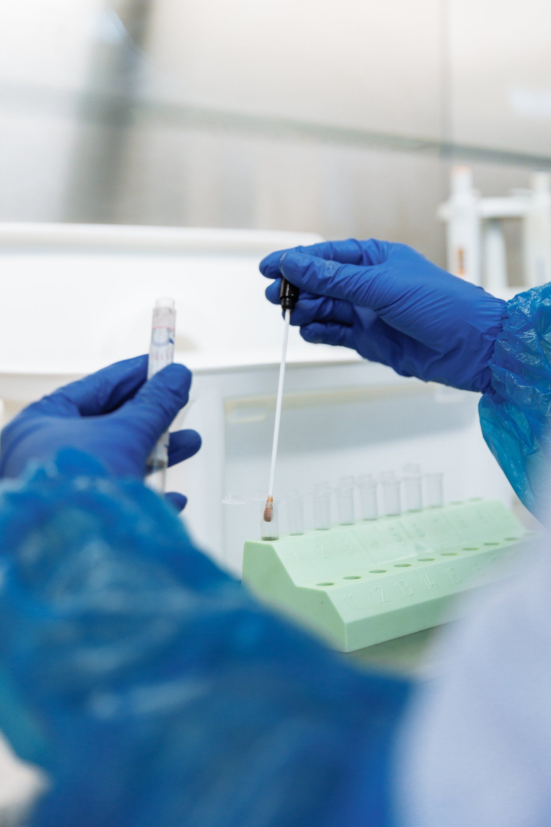 A person wearing blue gloves is holding a pipette and a test tube in a laboratory.