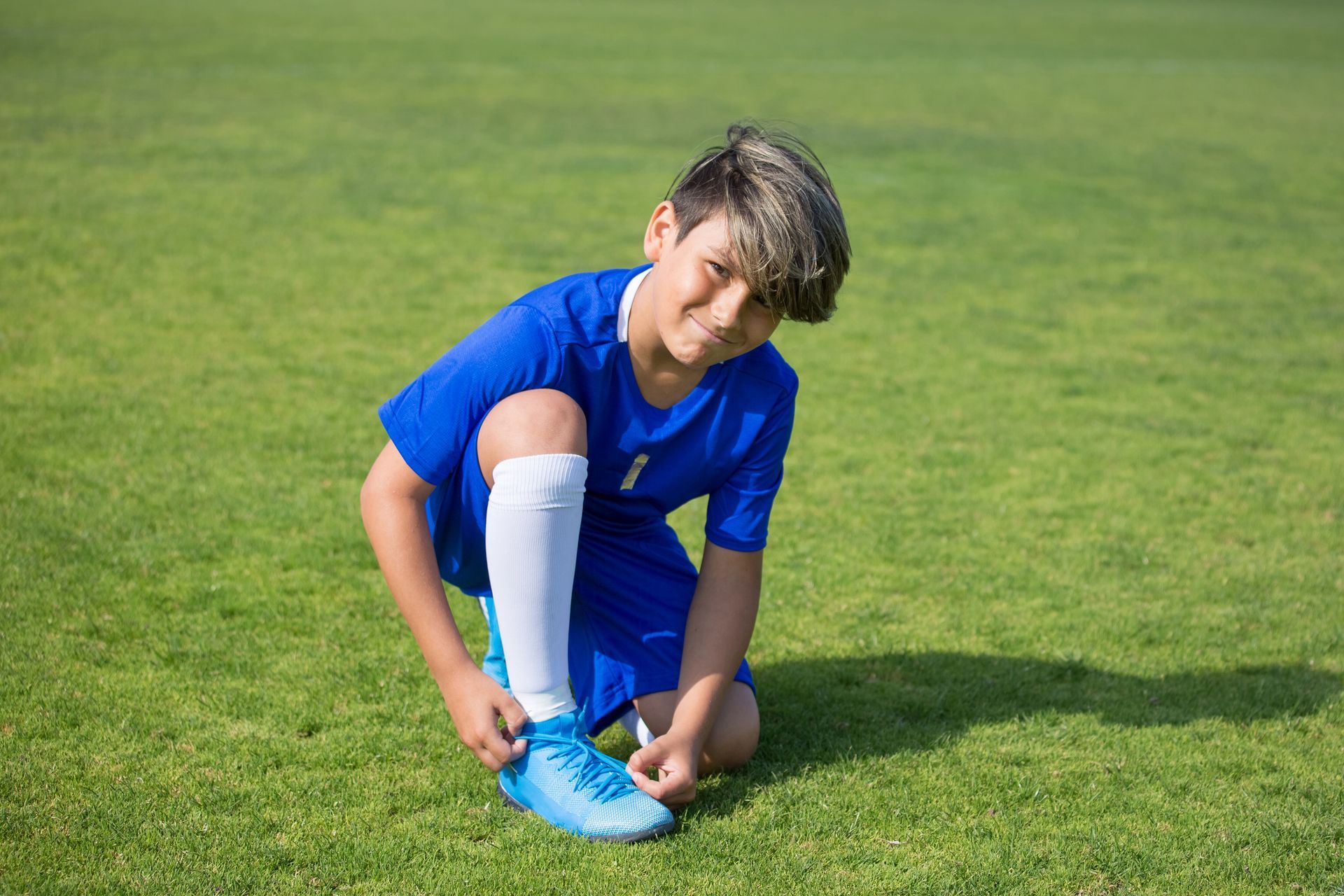 A young boy is tying his soccer cleats on a field.