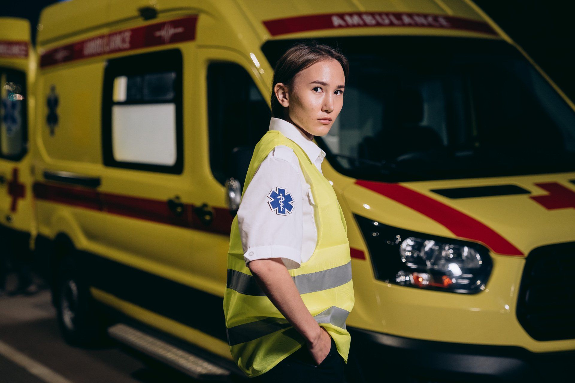 A photograph of a young Asian woman in a paramedic uniform standing in front of a yellow ambulance