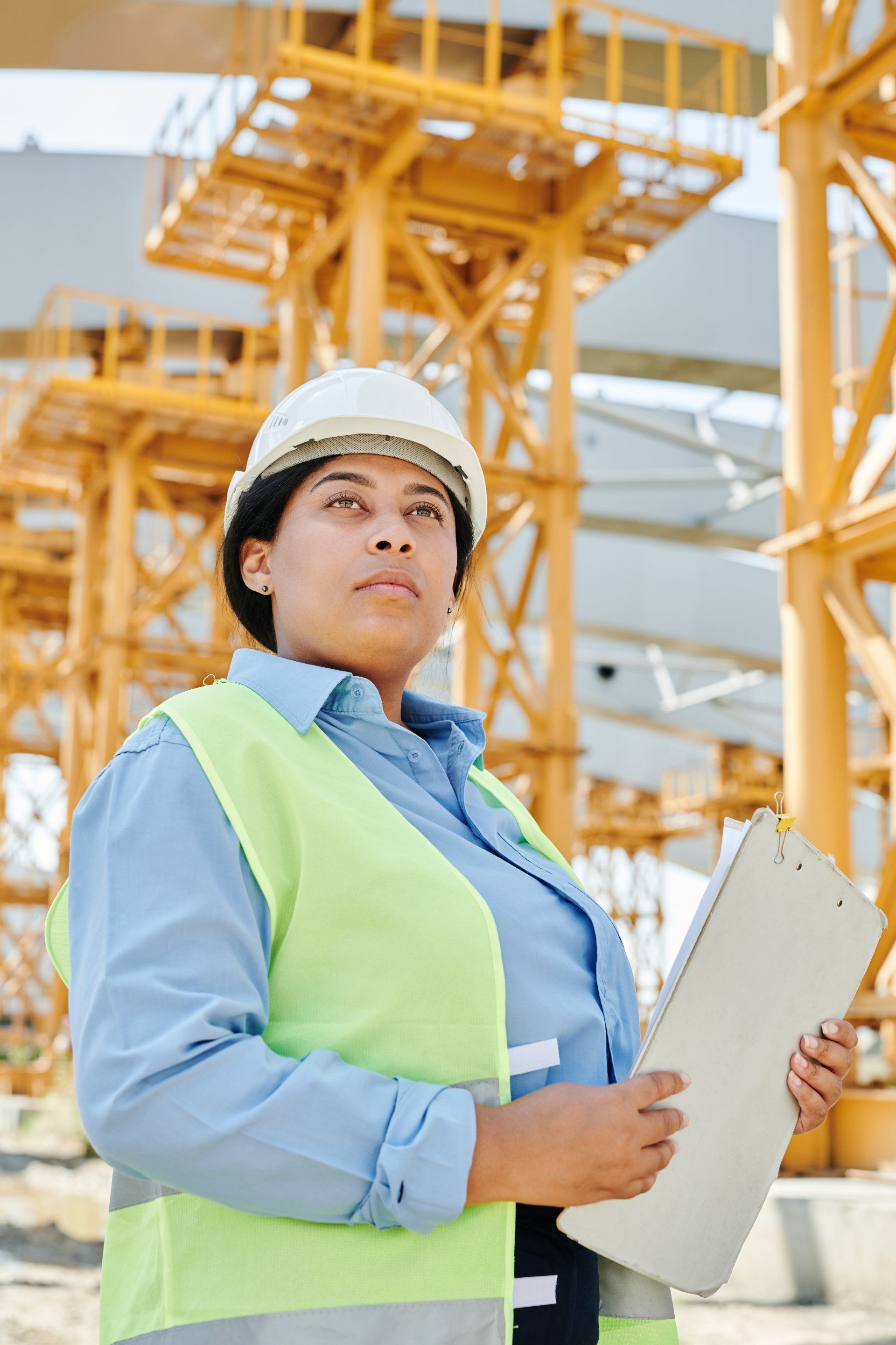 A woman is standing in front of a construction site holding a clipboard.