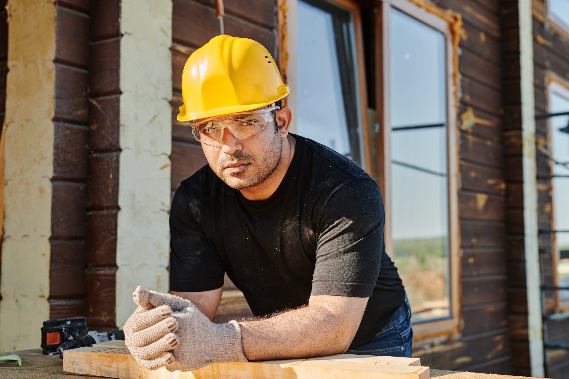 a man wearing a hard hat and safety glasses is leaning on a piece of wood .