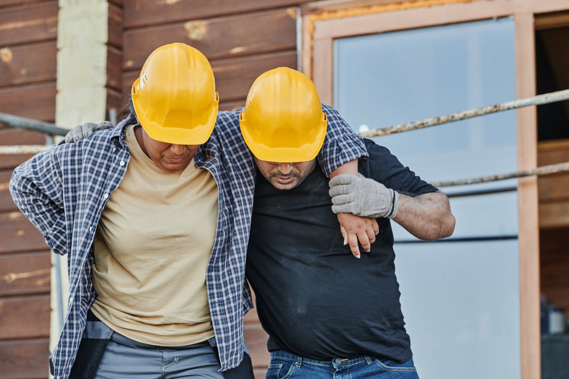 Two construction workers helping each other walk after an injury. 