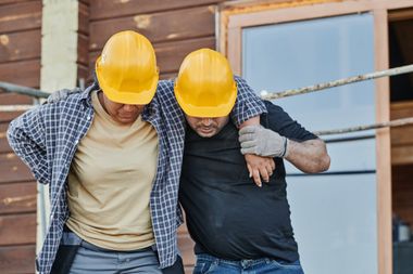 A man and a woman wearing hard hats are helping each other.