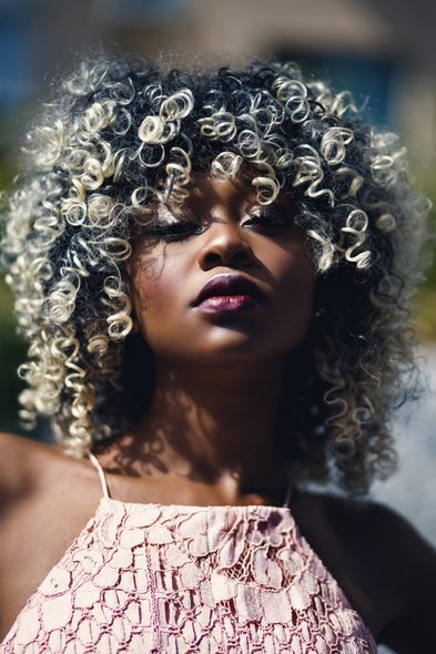 A woman with curly hair is wearing a pink dress and looking at the camera.