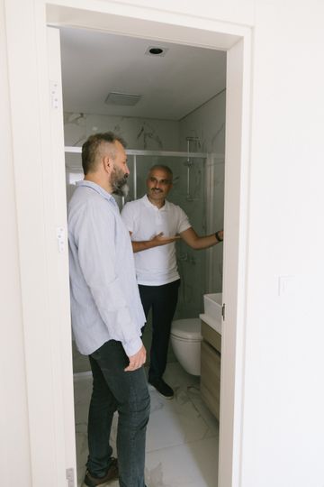 Two men are standing in a bathroom talking to each other.