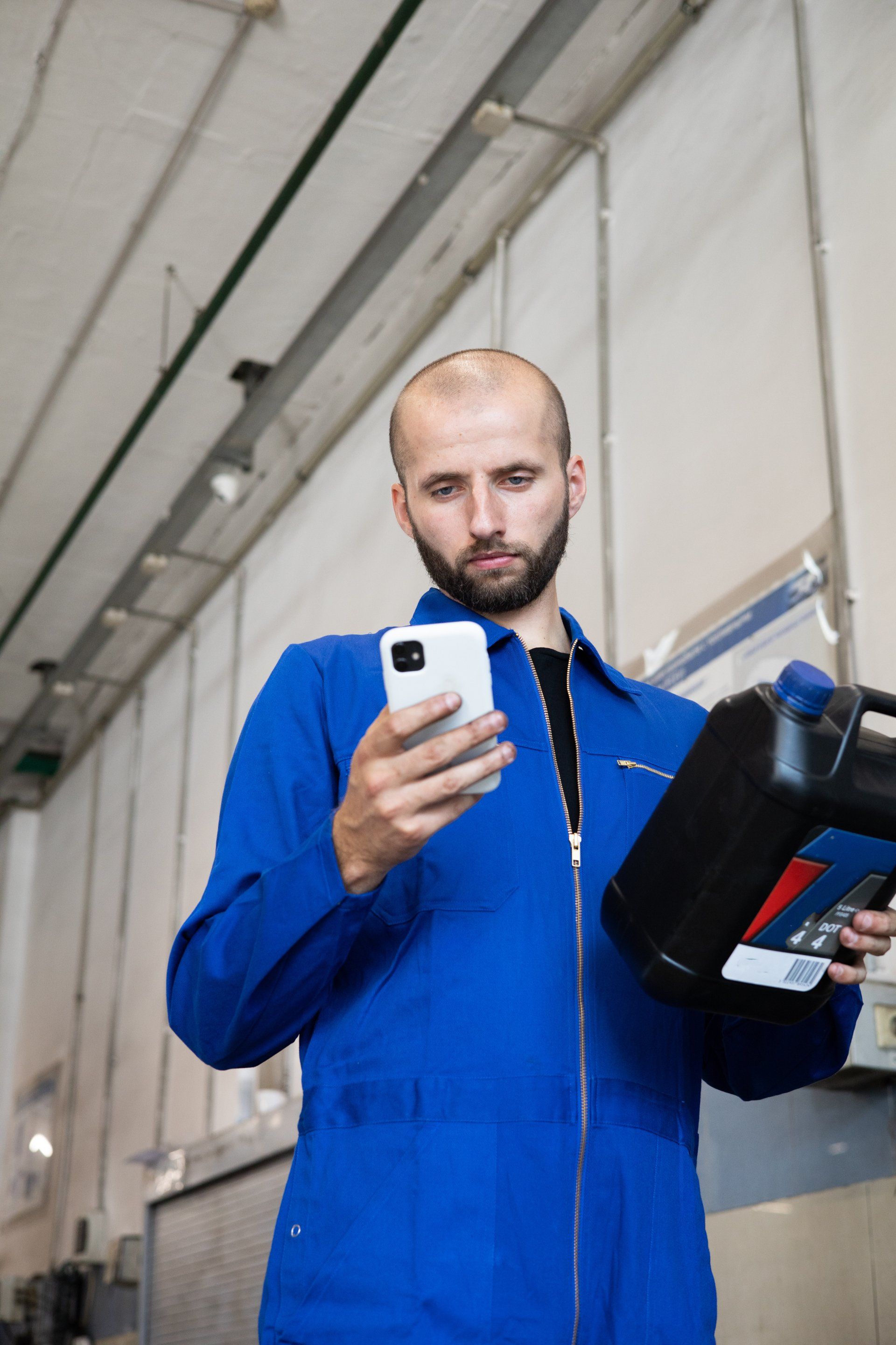 A man in a blue uniform is holding a bottle of oil and looking at his phone.