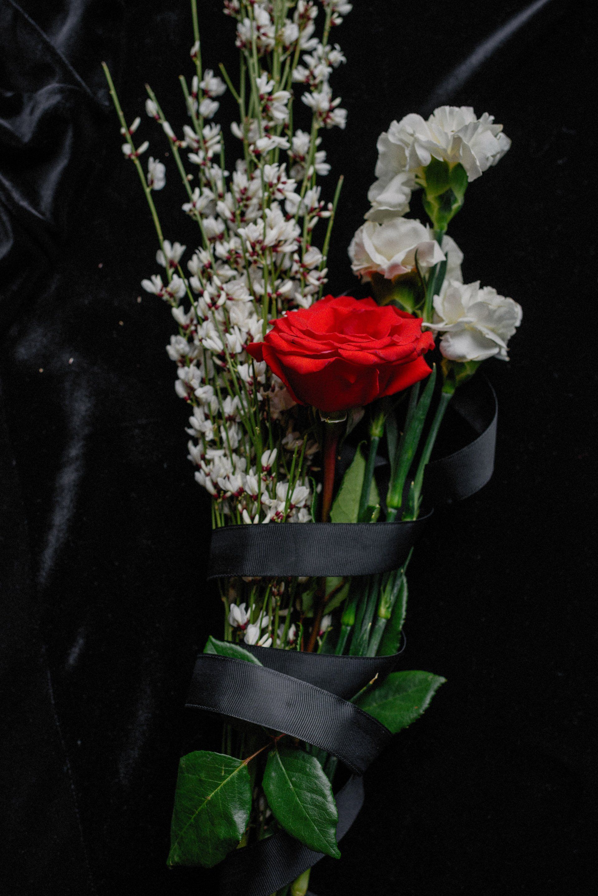 a bouquet of flowers with a red rose and white carnations wrapped in a black ribbon .