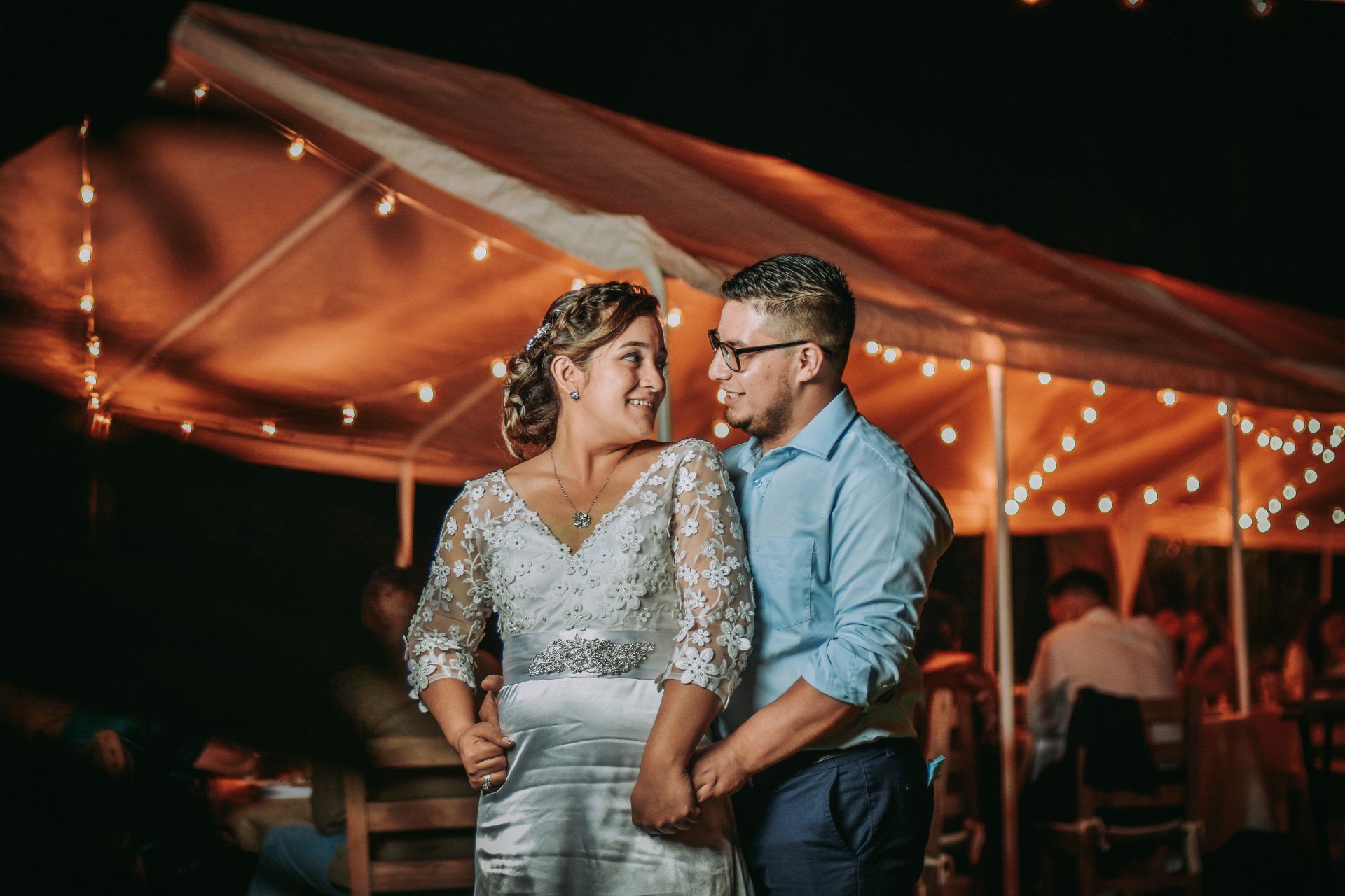 Close up of a bride and groom in front of a stretch tent with fairy lights in it.