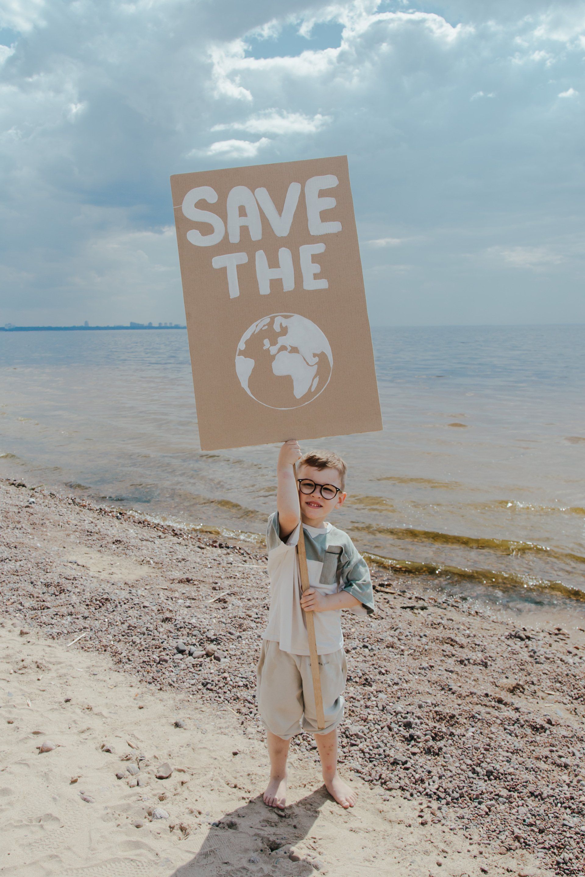 Little boy on a beach holding save the planet sign