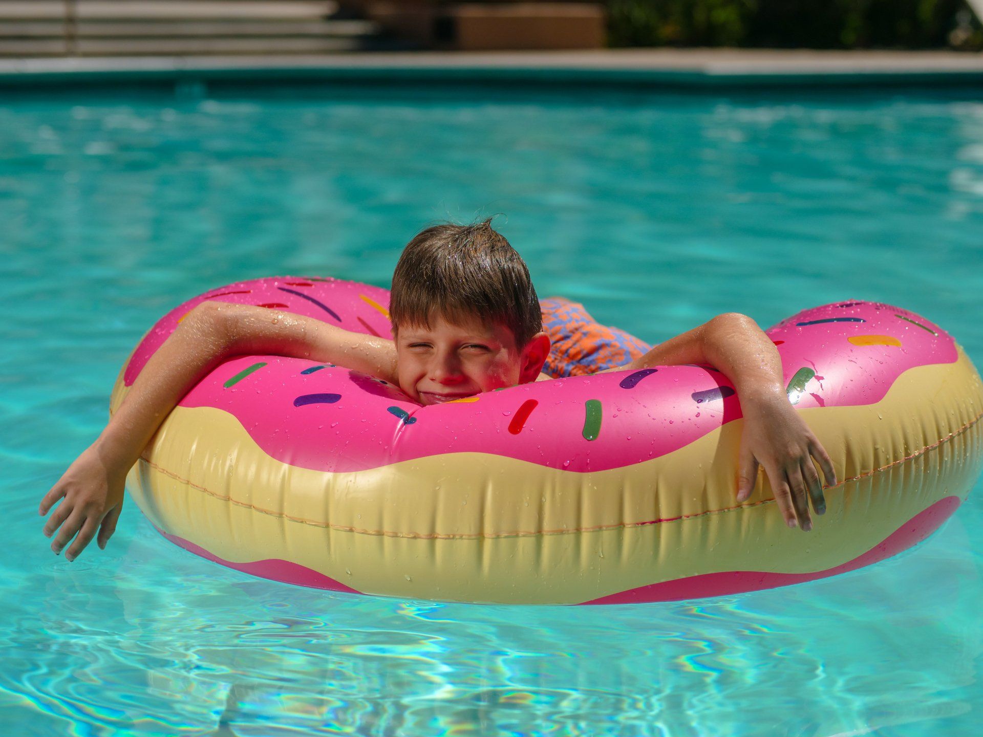 A young boy is floating on an inflatable donut in a swimming pool.