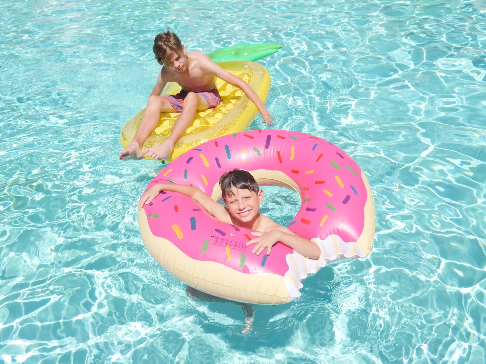 Two children are floating in a swimming pool with inflatable donuts.