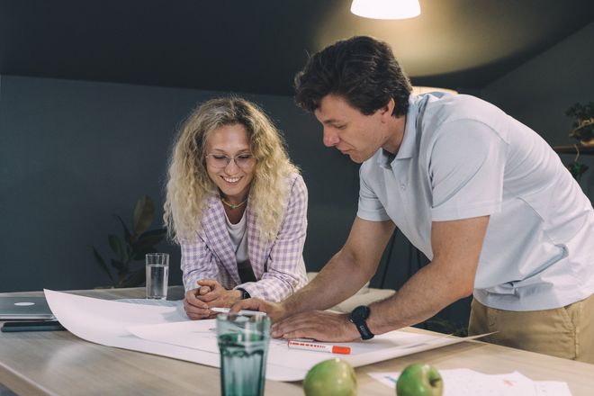 A man and a woman are looking at a blueprint on a table.