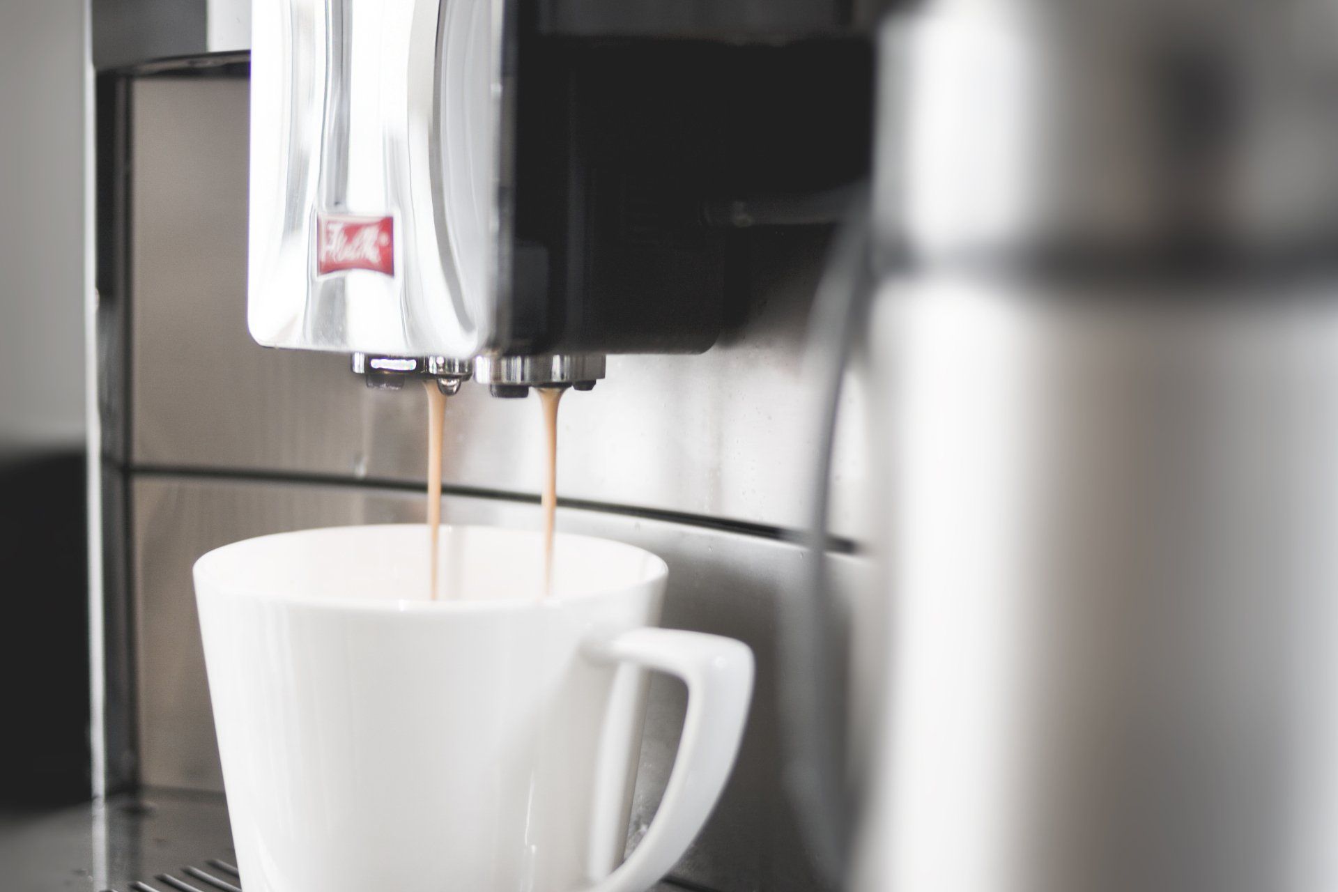 A cup of coffee is being poured from a coffee machine.