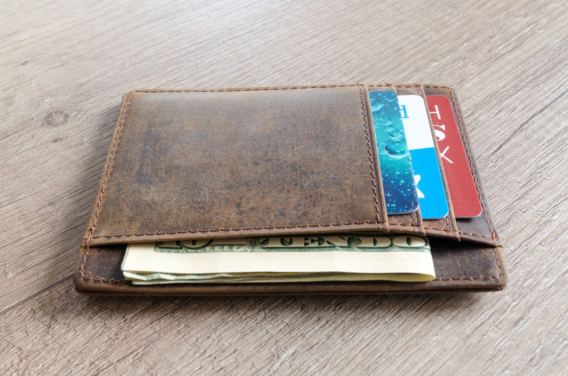 An image a faded, brown leather wallet with visible dollar bills and credit cards in the pockets.