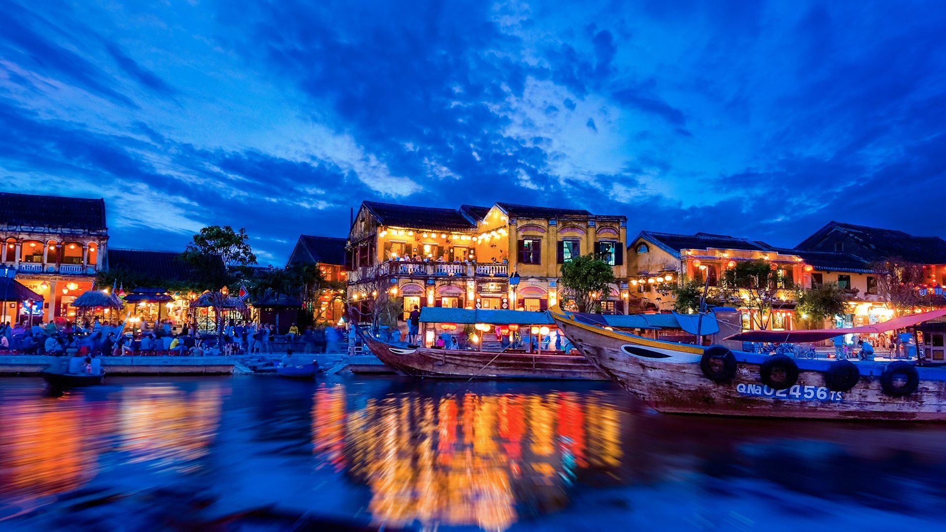 A city at night with boats in the water and buildings reflected in the water.