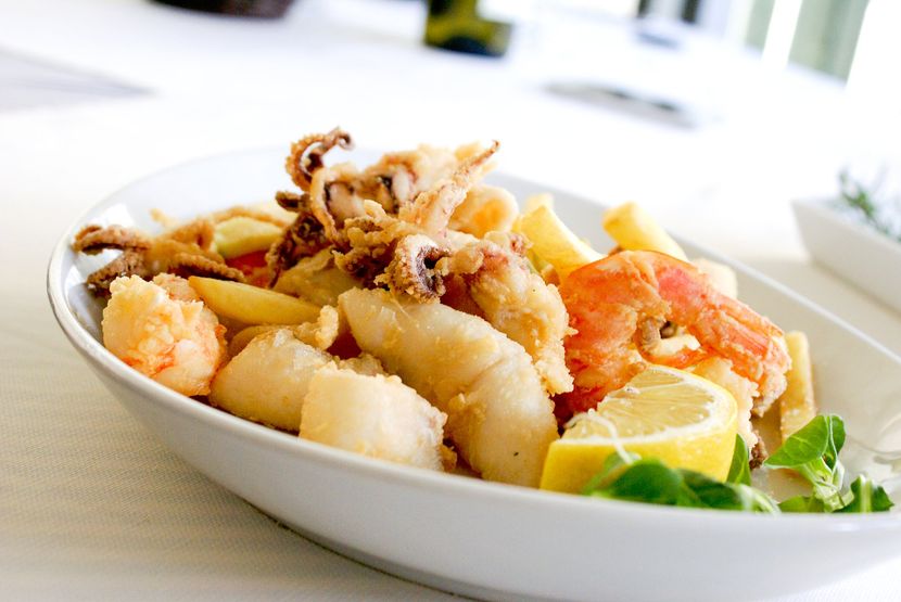 A white bowl filled with fried seafood and french fries on a table.